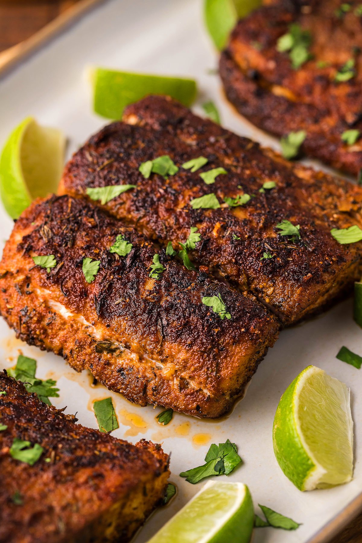 Blackened cajun seasoned fish fillets garnished with chopped herbs and served with lime wedges on a white plate, cooked to perfection in a cast iron skillet.