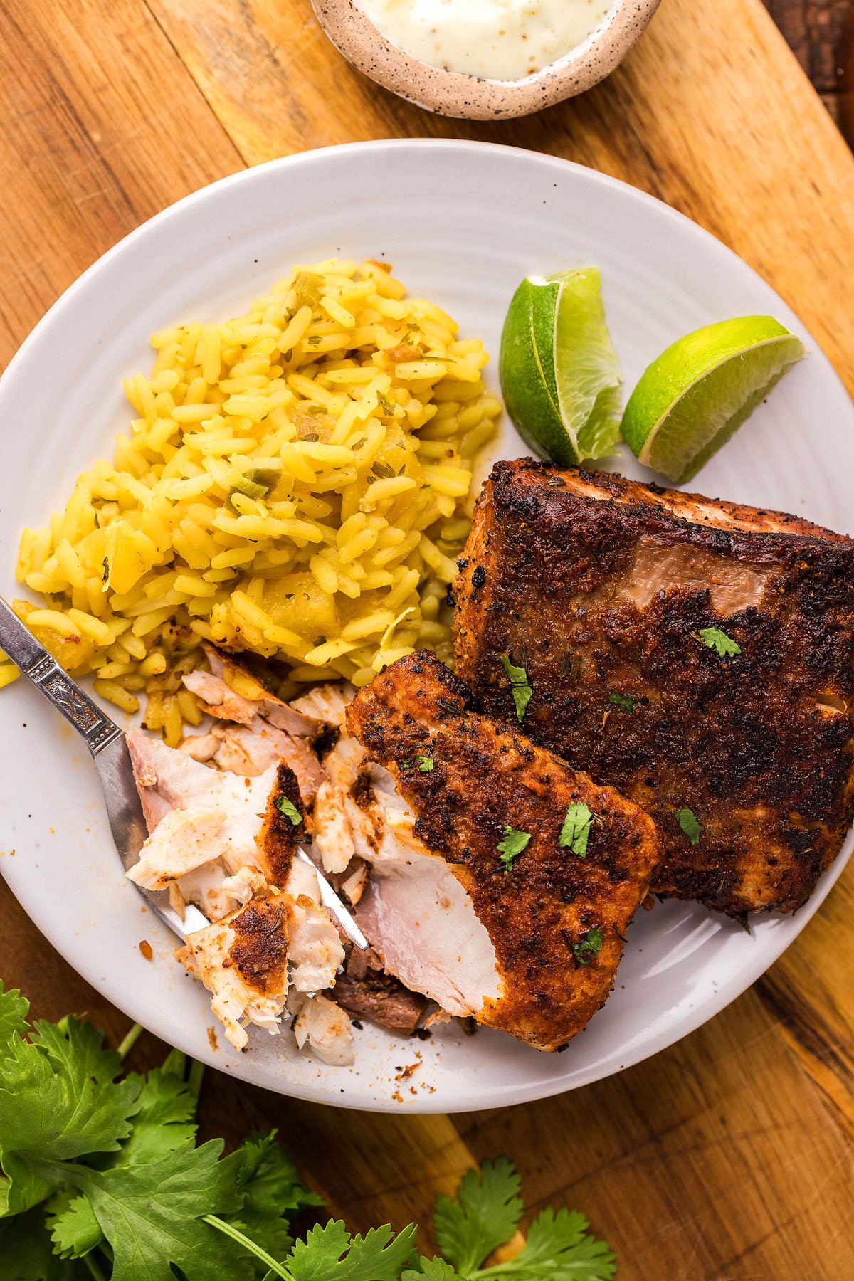 A plate with yellow rice, two pieces of cajun seasoned fish cooked in a cast iron skillet, lime wedges, and a fork breaking the fish.