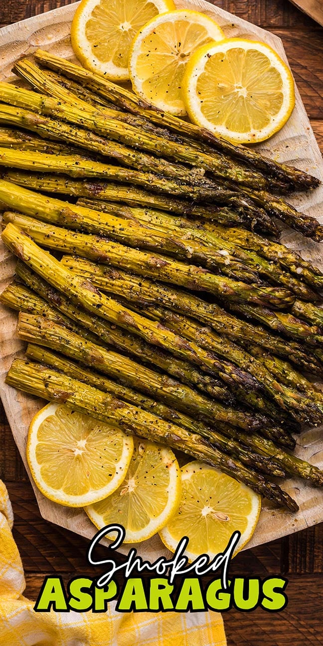 Grilled asparagus spears on a wooden board, garnished with lemon slices and pepper.