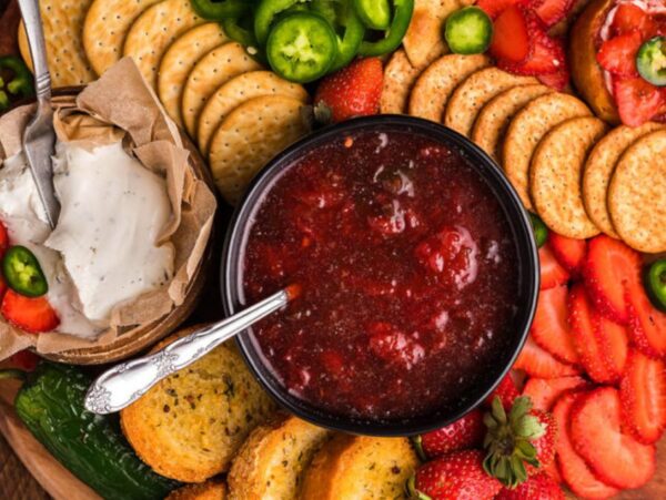 A delightful cheese or charcuterie board featuring crackers, cream cheese, Strawberry Jalapeño Jam, fresh strawberries, jalapeños, and toasted bread—perfect for sharing.