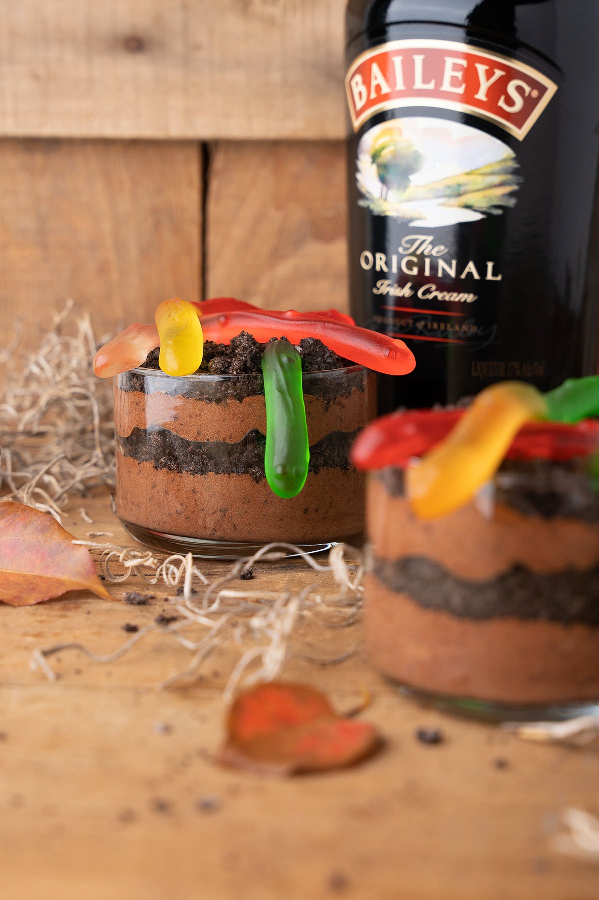 These Boozy Dirt Cups feature chocolate mousse, crushed cookies, gummy worms, and a bottle of Baileys Irish Cream nearby for a fun twist on classic worm and dirt parfaits—perfect for dessert cocktails lovers!.