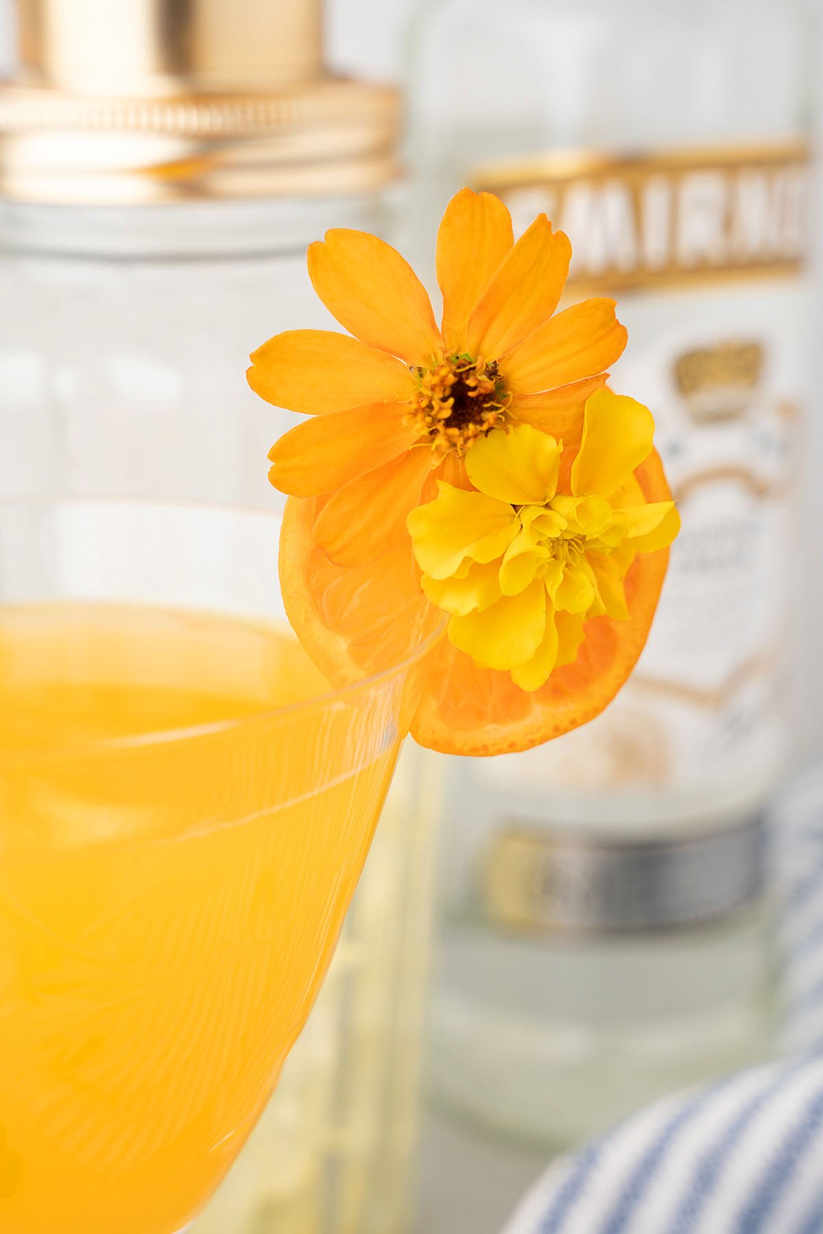 A Clementine Martini garnished with orange and yellow flowers, with bottles blurred in the background, makes the perfect summer cocktail.