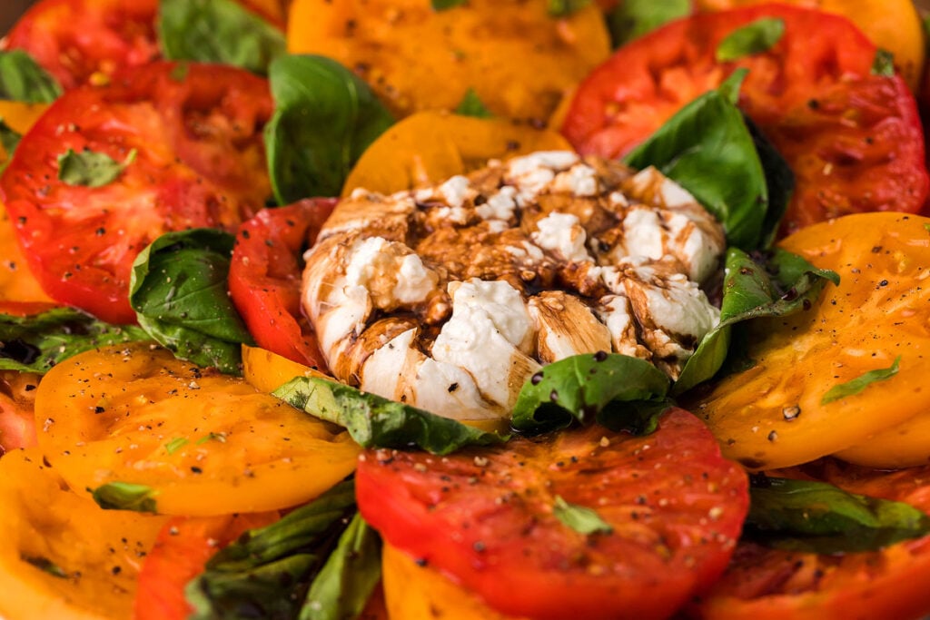 Sliced red and yellow tomatoes with basil, topped with burrata cheese and balsamic glaze.