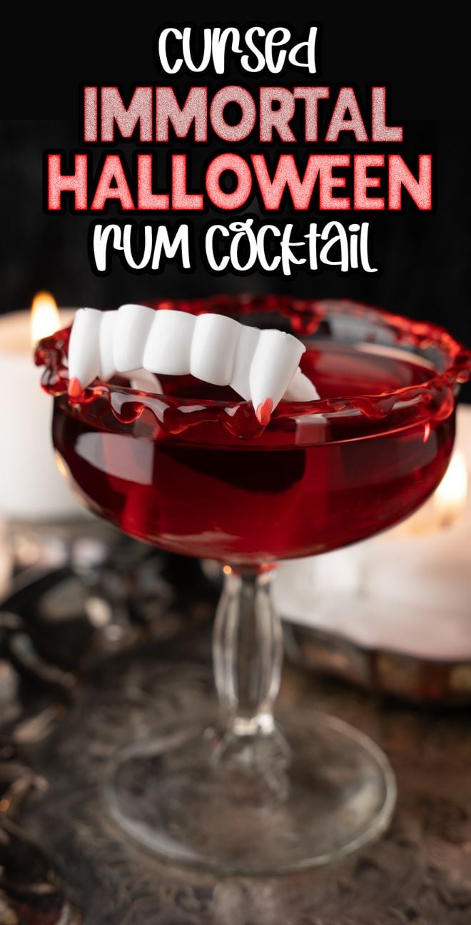 A blood red cocktail in a glass with fake vampire fangs and red syrup, surrounded by candles—a Cursed Immortal Halloween Rum Cocktail that's the perfect party beverage for spooky nights.