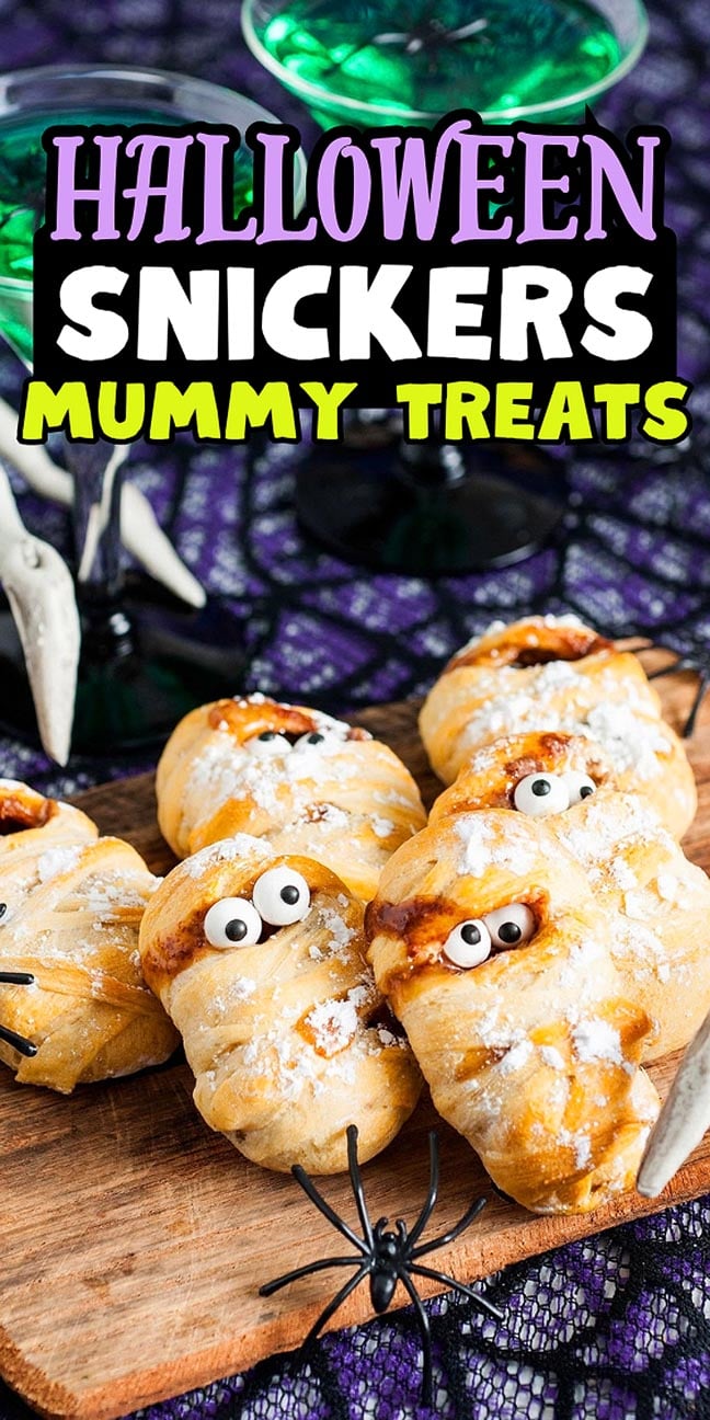 Halloween Snickers mummy treats with candy eyes on a wooden board.