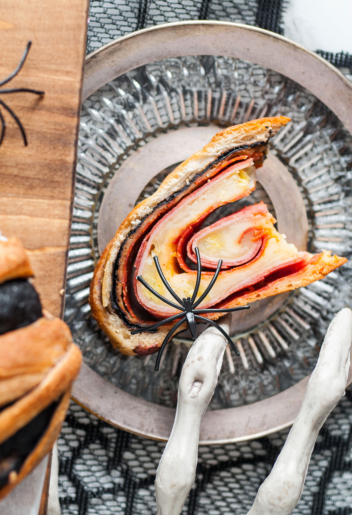 A slice of homemade stromboli made with Pillsbury refrigerated pizza dough sits on a plate, topped with a black plastic spider for a spooky Halloween Mummy Stromboli Dinner.