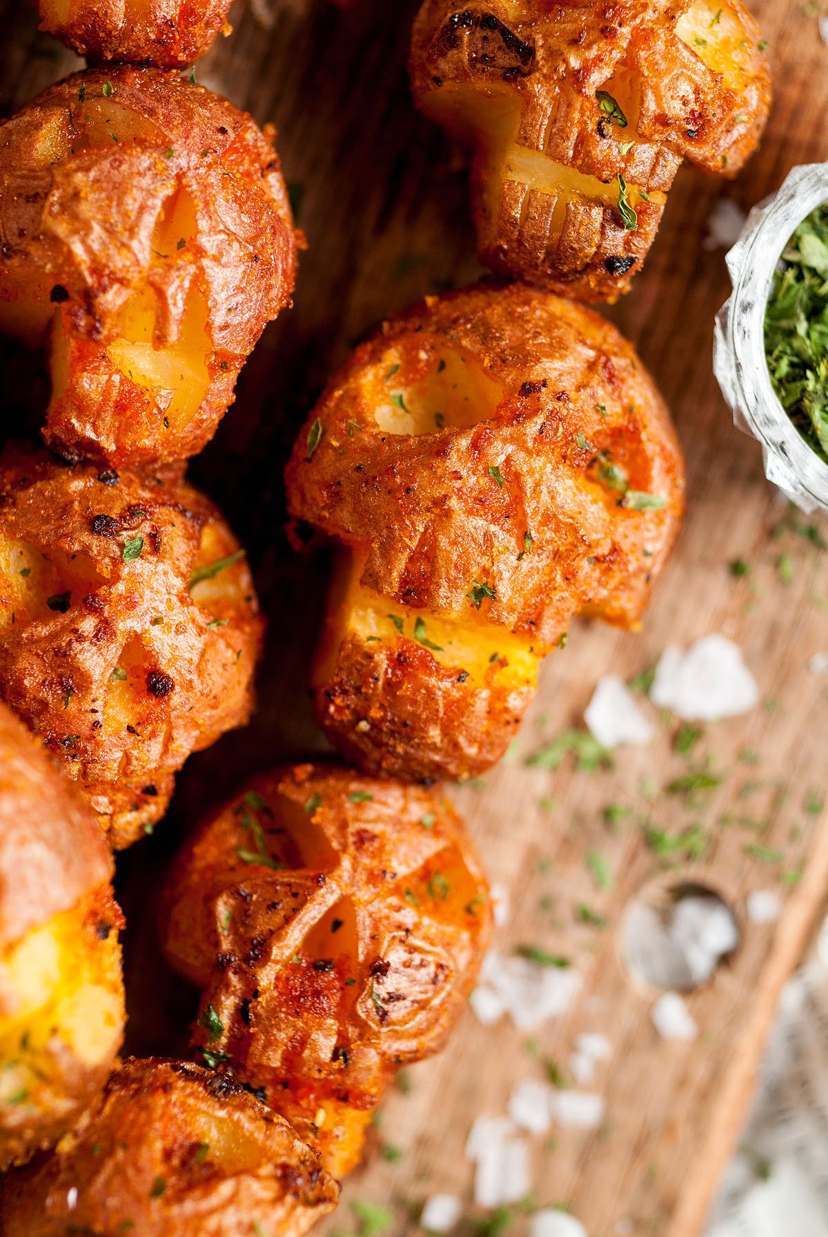 Crispy roasted potatoes with herbs on a wooden surface, sprinkled with salt and chopped parsley—perfect as a Halloween side dish or appetizer to complete your spooky celebration.
