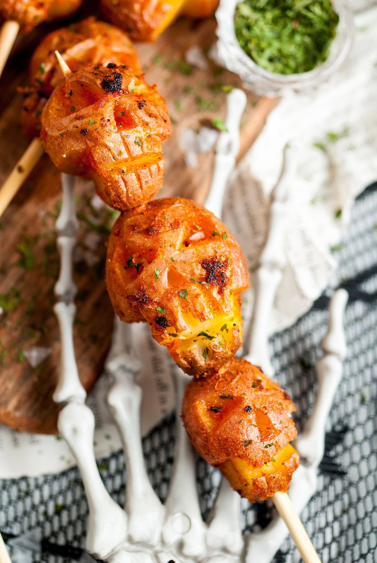 Grilled, shrunken head potato skewers on a skeleton hand serving tray, garnished with herbs for the perfect spooky potatoes.