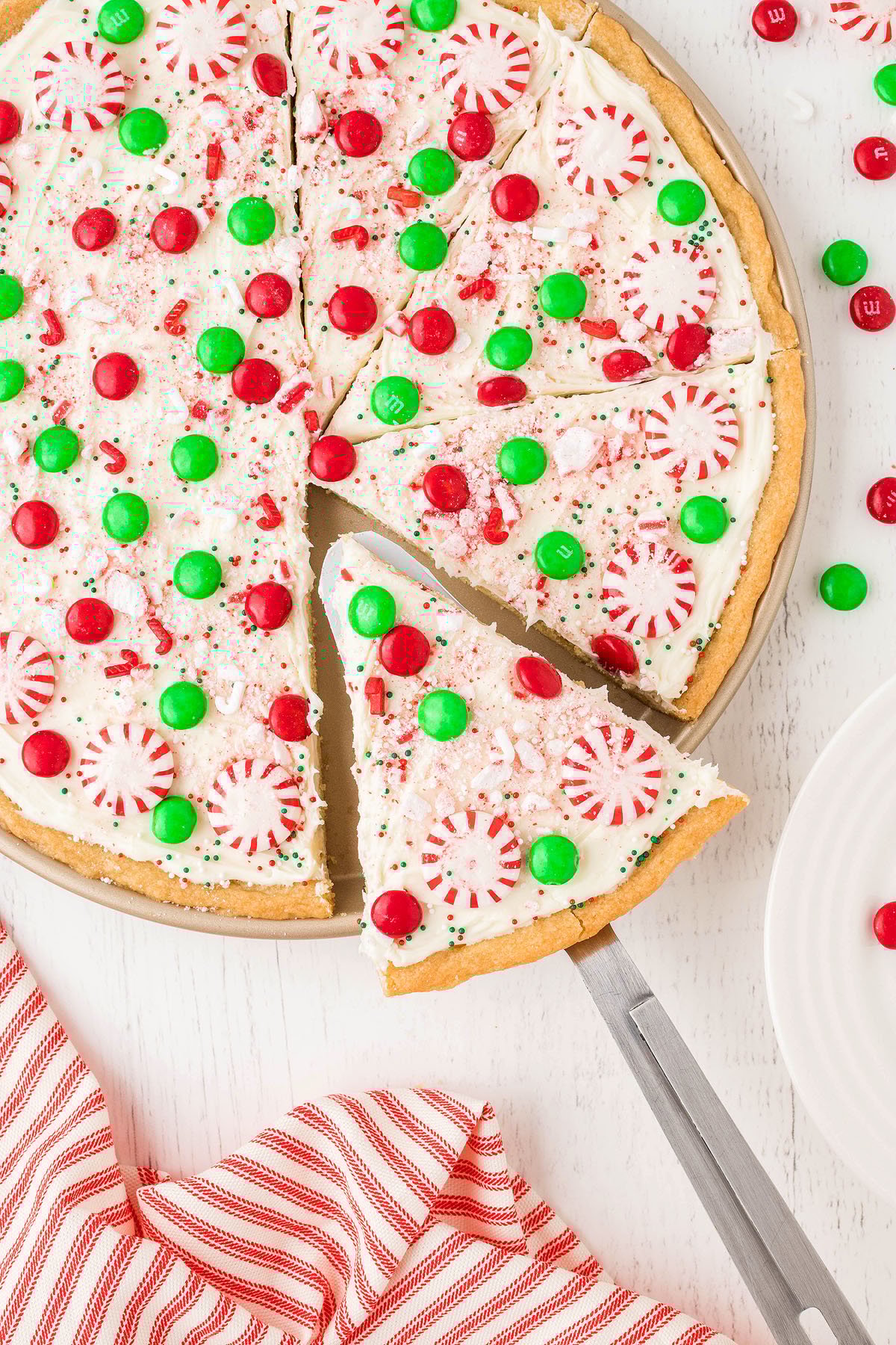 Enjoy a Holiday Cookie Pizza made with refrigerated sugar cookie dough, topped with white frosting, red and green candies, and peppermint candies—a perfect Christmas dessert pizza for festive gatherings!.