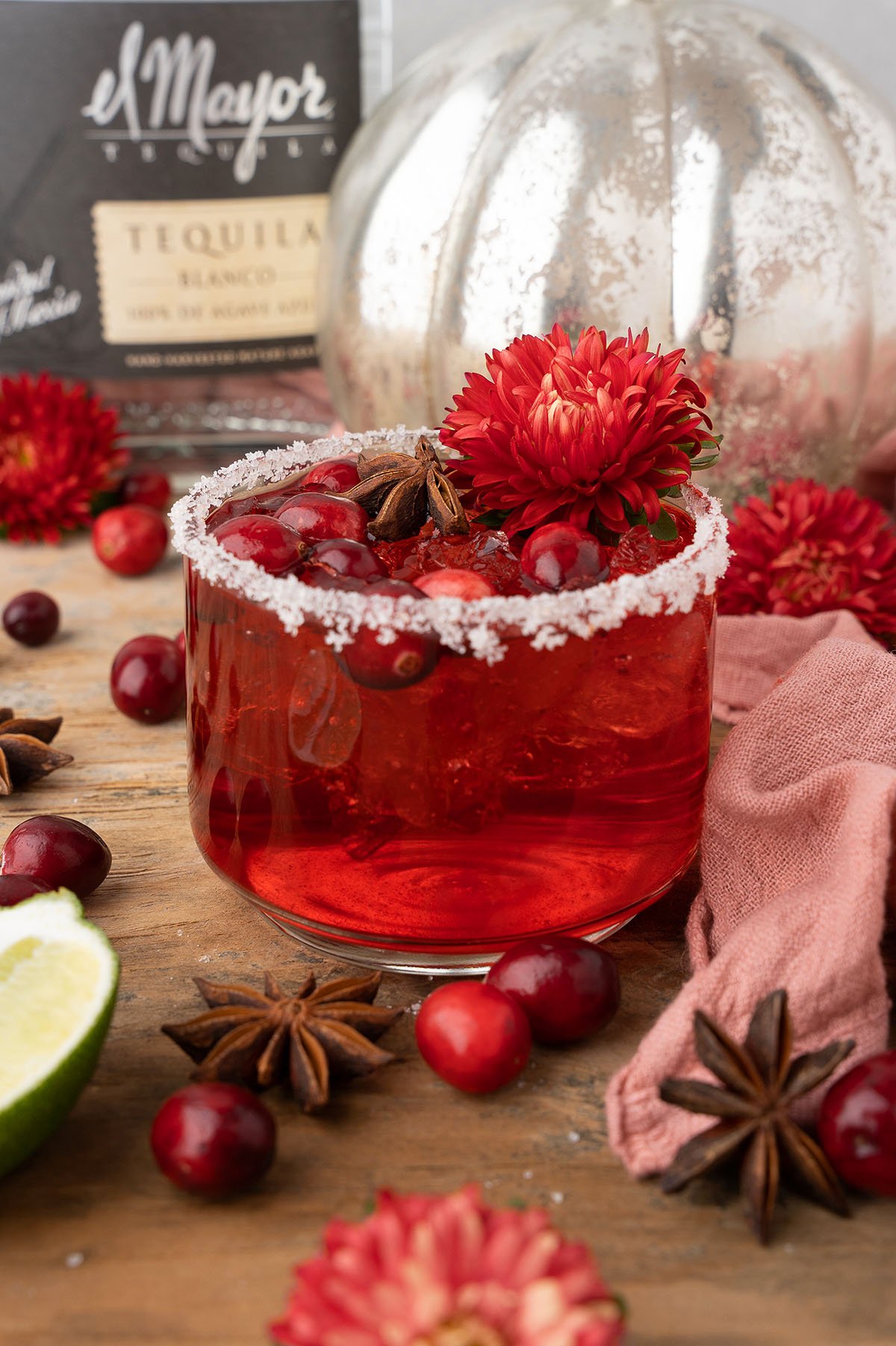 A festive red cocktail with ice, cranberries, and flowers in a salt-rimmed glass, surrounded by star anise—this Thanksgiving or Christmas cocktail shines with Silver tequila and triple sec.