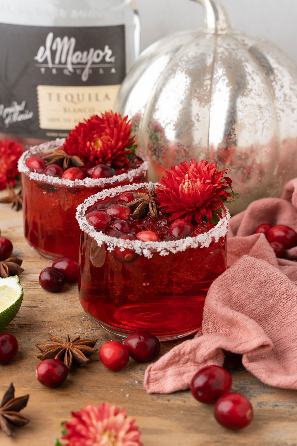 Two red Holiday Cranberry Margaritas with sugared rims, garnished with cranberries, star anise, and red flowers on a wooden table—perfect for showcasing your favorite holiday margarita recipe with Silver tequila and triple sec.