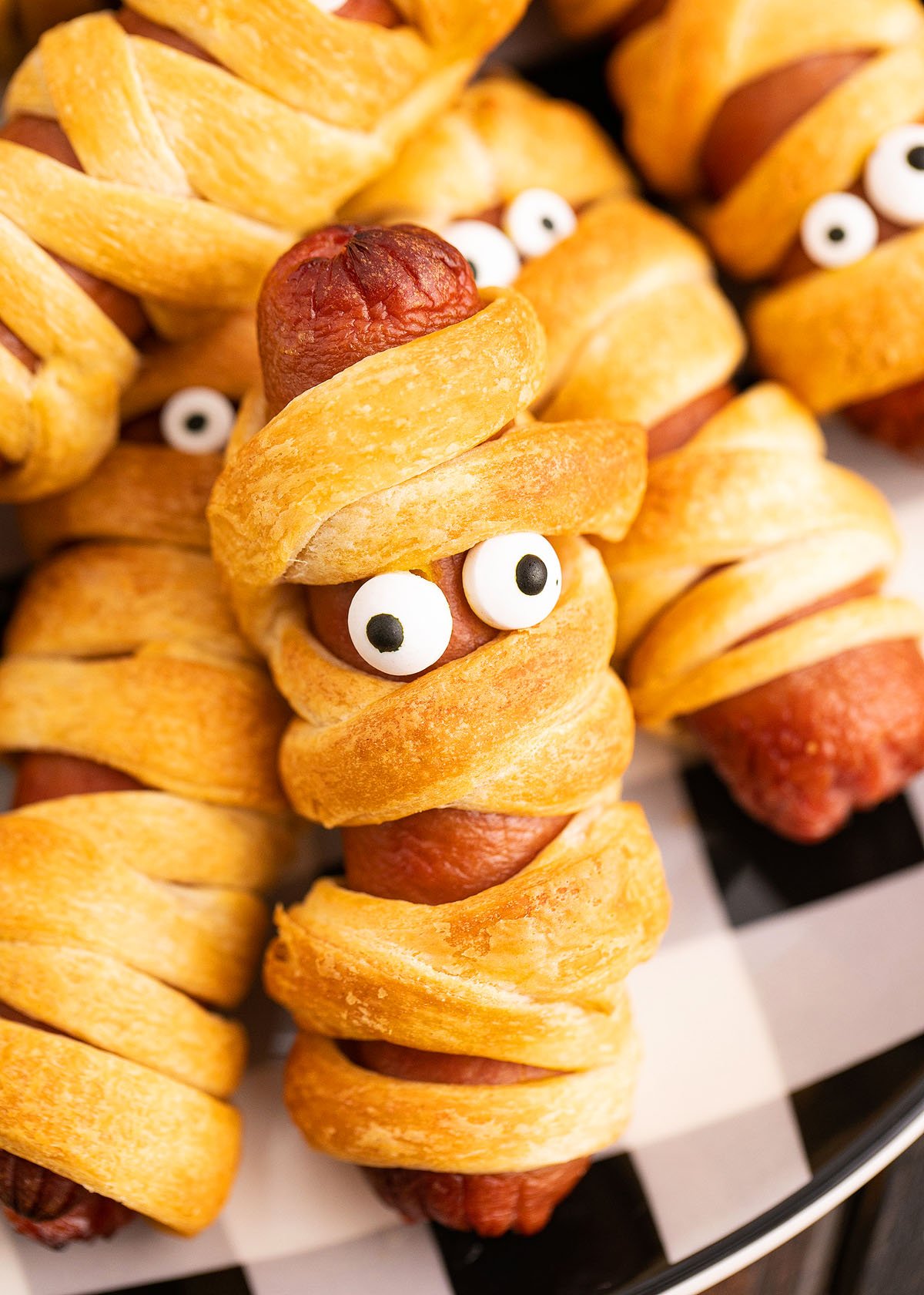 Crescent roll hot dog mummies are spooky pigs in a blanket, wrapped to look like mummies with candy eyes, served on a black and white plate—perfect for your Halloween party!.