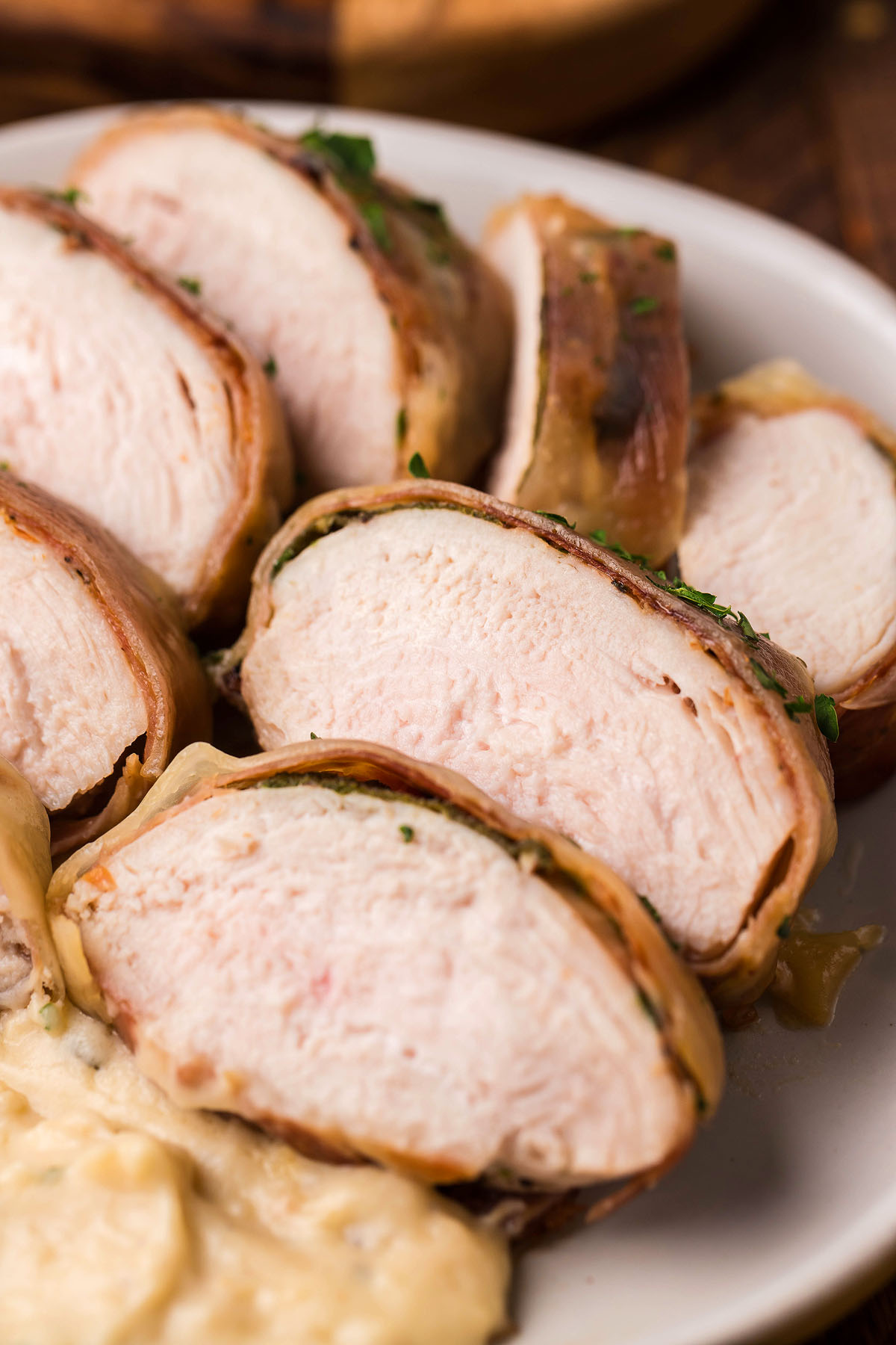 Sliced bacon-wrapped chicken breast on a white plate, served with a creamy sage saltimbocca sauce for an easy dinner recipe.