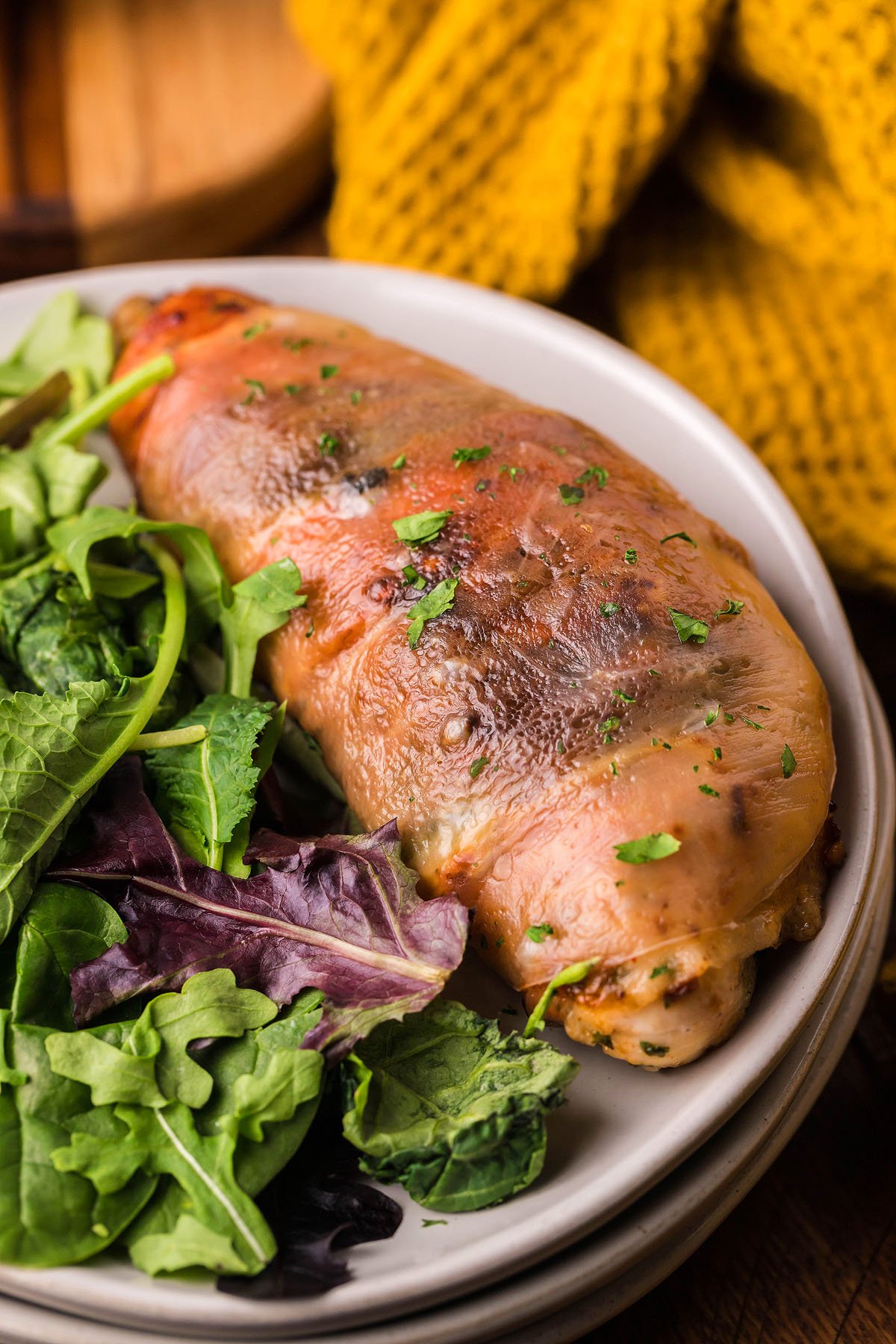 Stuffed chicken breast with herbs and prosciutto, inspired by classic Chicken Saltimbocca, served alongside a fresh green salad on a white plate.
