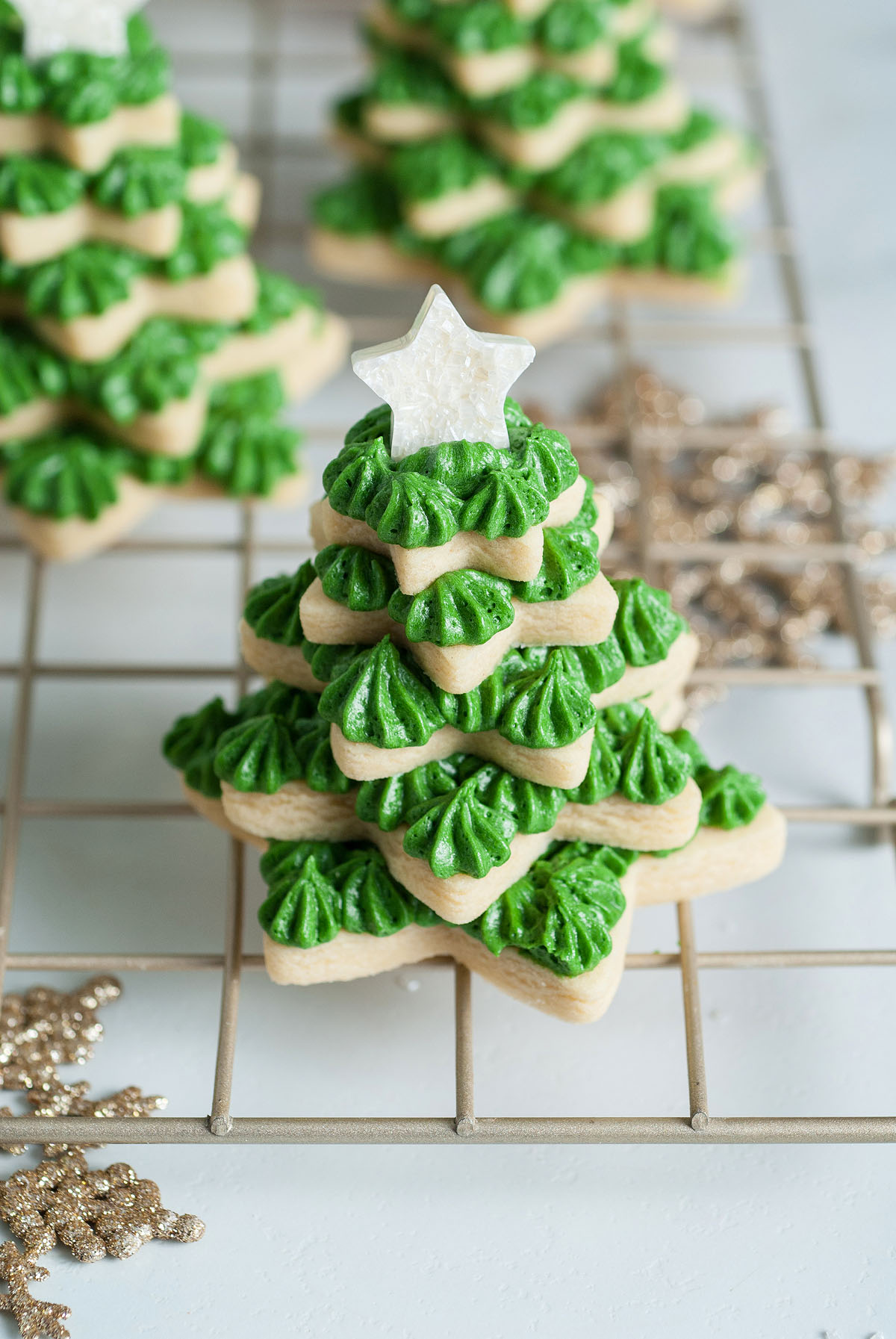 Christmas sugar cookies shaped with star cookie cutters are stacked to form a festive cookie tree, topped with a star and green icing, displayed on a cooling rack.