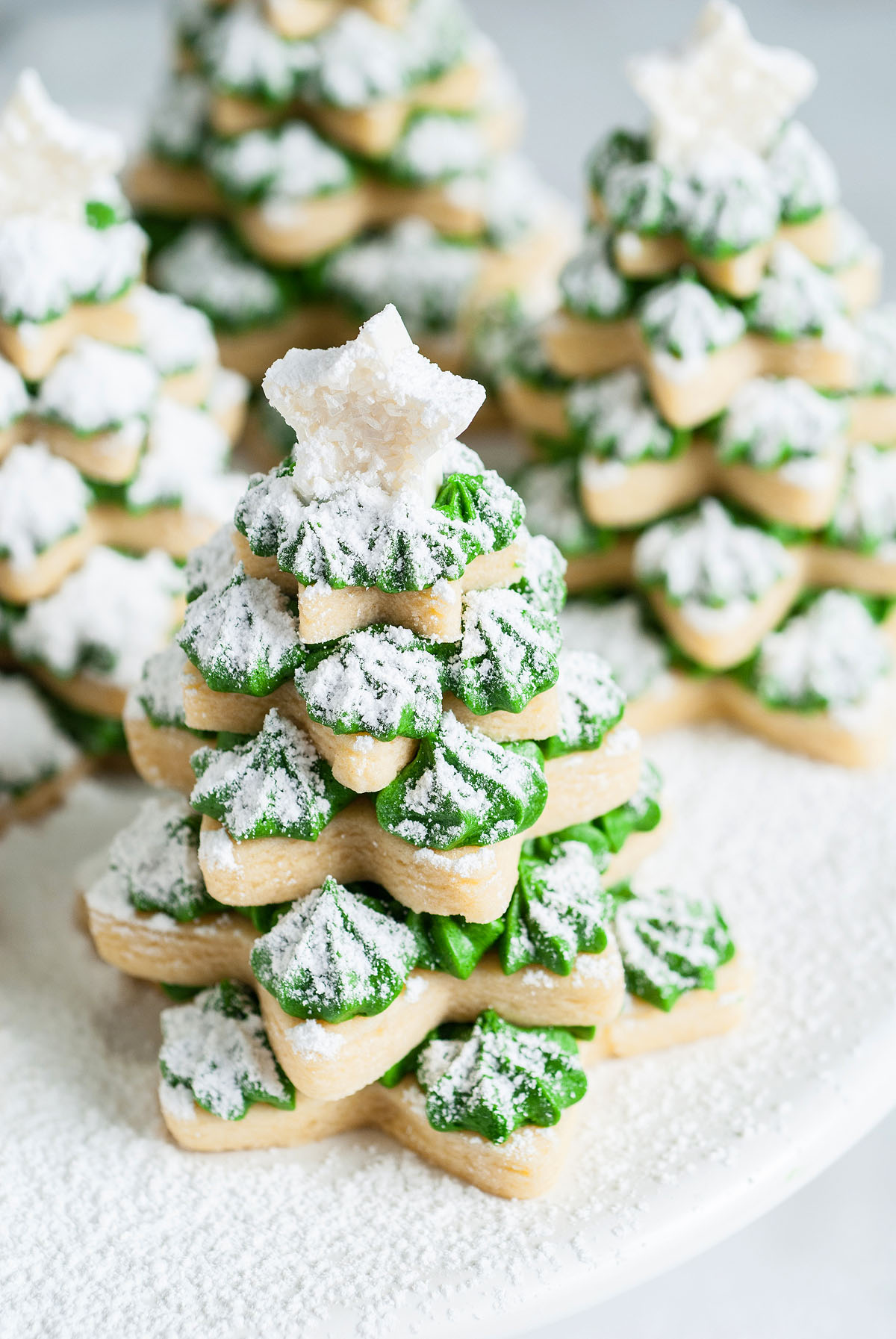 Stacked 3D Christmas Tree Sugar Cookies with green icing, powdered sugar, and a white star on top. Crafted in festive tree shapes using star cookie cutters for a delightful holiday treat.