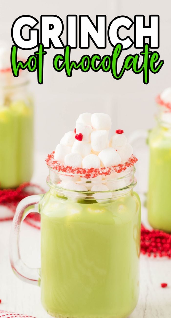 A glass mug of Green Grinch hot chocolate, topped with marshmallows and red candy hearts. Text reads "Grinch Hot Chocolate.