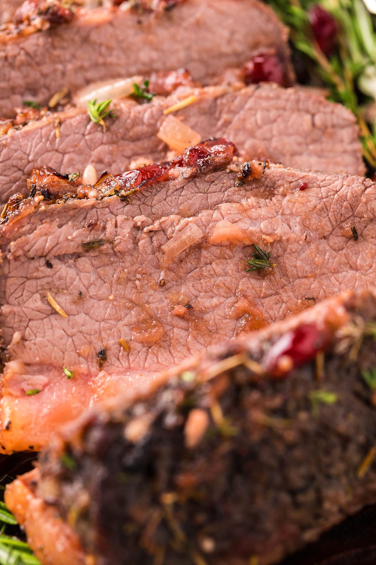 Close-up of juicy, sliced Cranberry Holiday Beef Brisket, with herbs and seasonings visible on the surface—a festive twist on a classic beef brisket recipe.