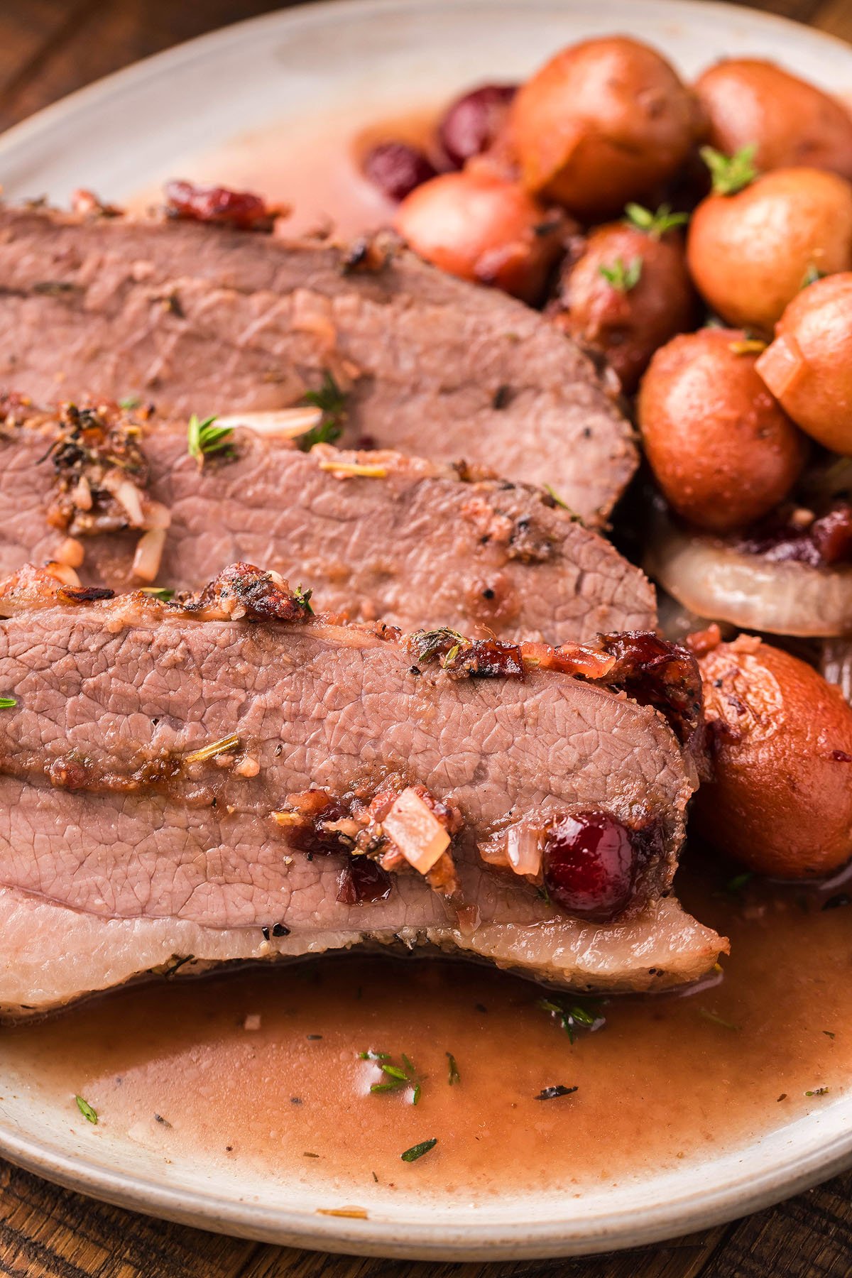 Sliced Cranberry Holiday Beef Brisket with sauce, served alongside small red potatoes—a perfect choice for a festive holiday meal or thanksgiving or christmas dinner.