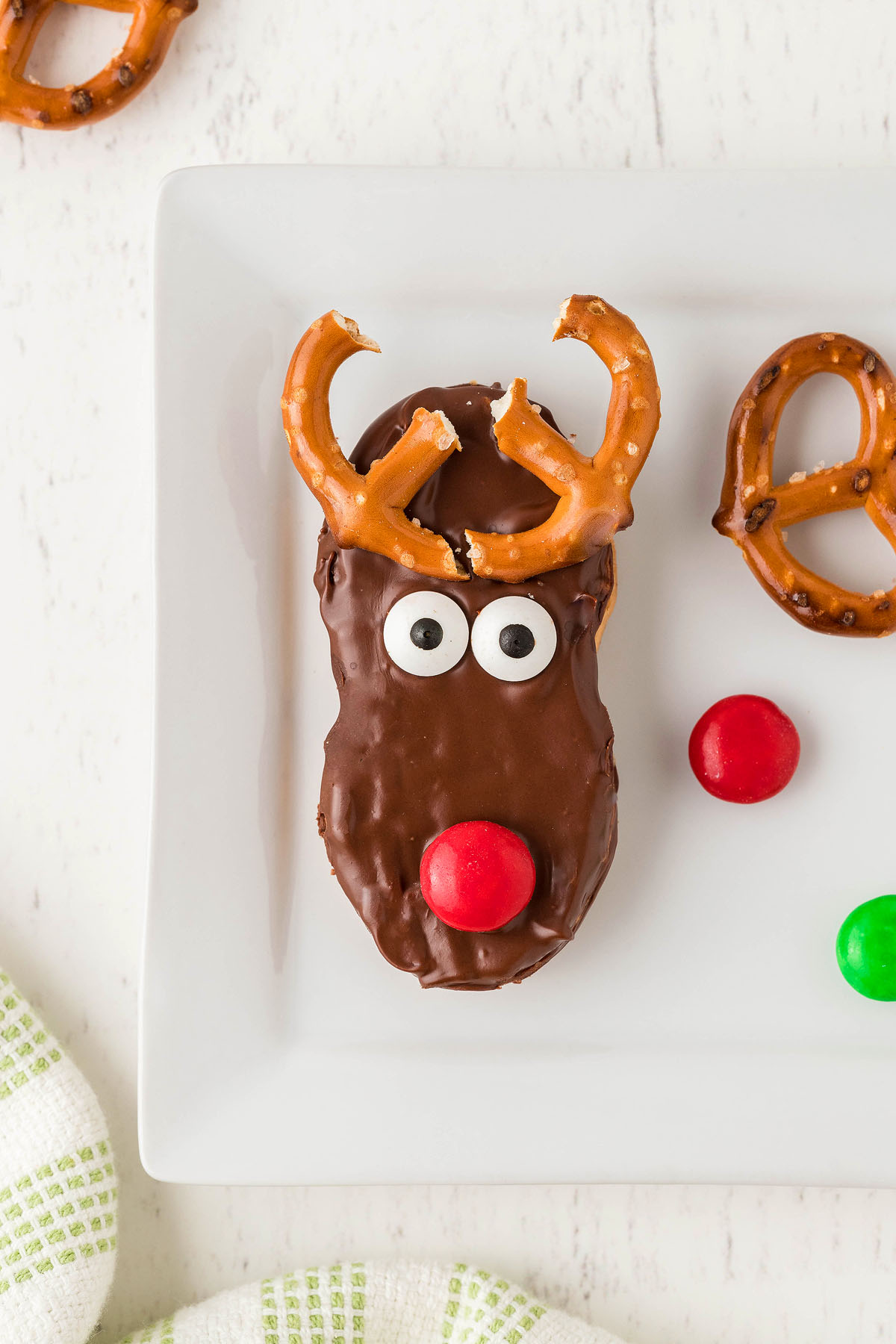 A Nutter Butter Reindeer Cookie with chocolate coating, pretzel antlers, candy eyes, and a red candy nose sits on a white plate—one of the cutest Christmas treats you'll find this season!.