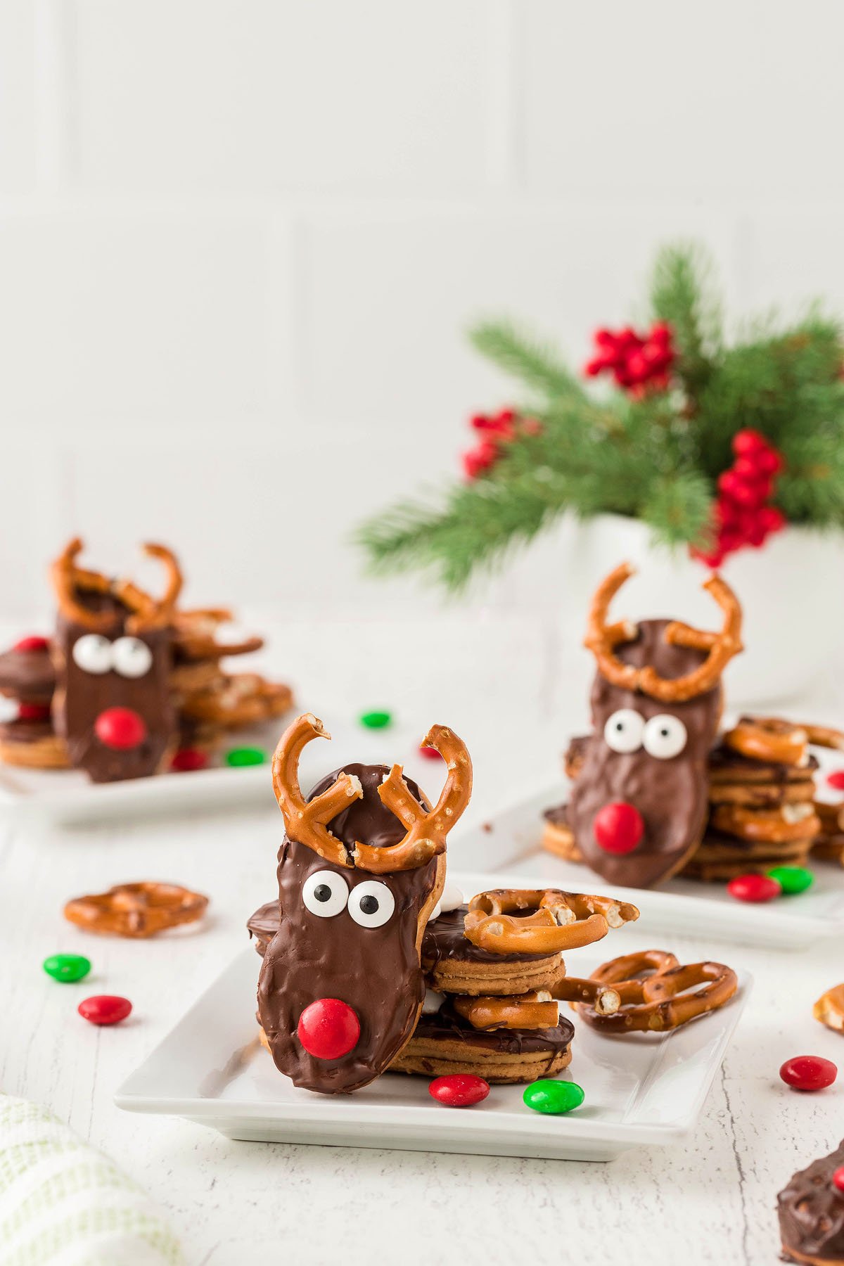 Nutter Butter Reindeer Cookies with pretzel antlers, candy eyes, and red noses make adorable Christmas treats, perfect for holiday parties and festive gatherings. Served on white plates with holiday decor.
