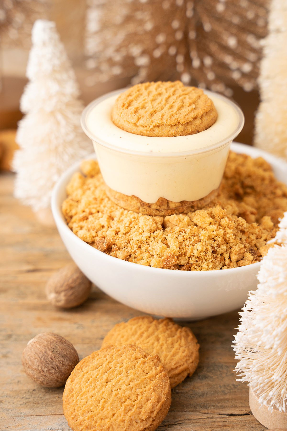 A bowl of cookie crumble topped with creamy dessert and a whole cookie, surrounded by festive decor, makes the perfect companion to Ginger Snap Eggnog Pudding Shots for a truly indulgent holiday treat.