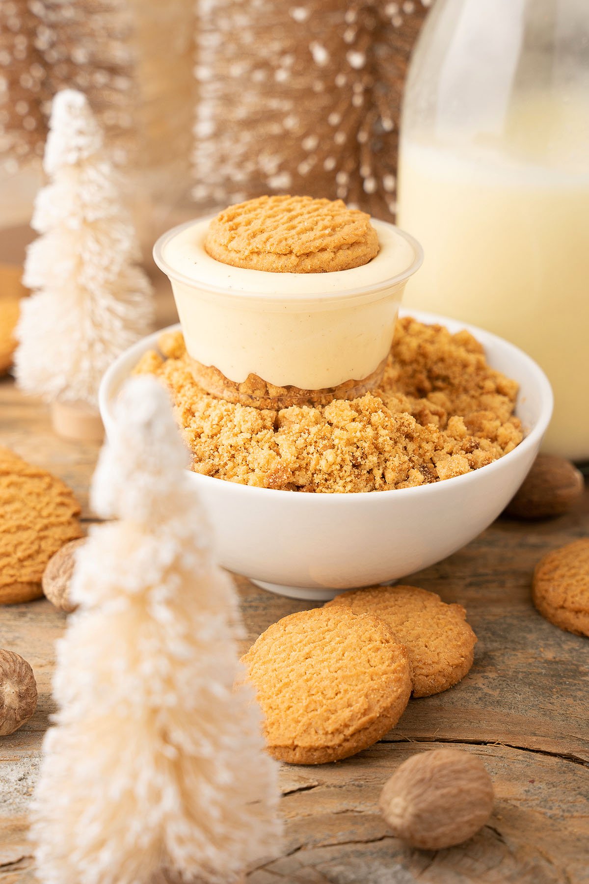 A bowl of cookie crumble dessert topped with custard and a cookie, surrounded by cookies and festive decor—perfect for serving as boozy pudding cups with Black spiced rum and RumChata during the holidays.