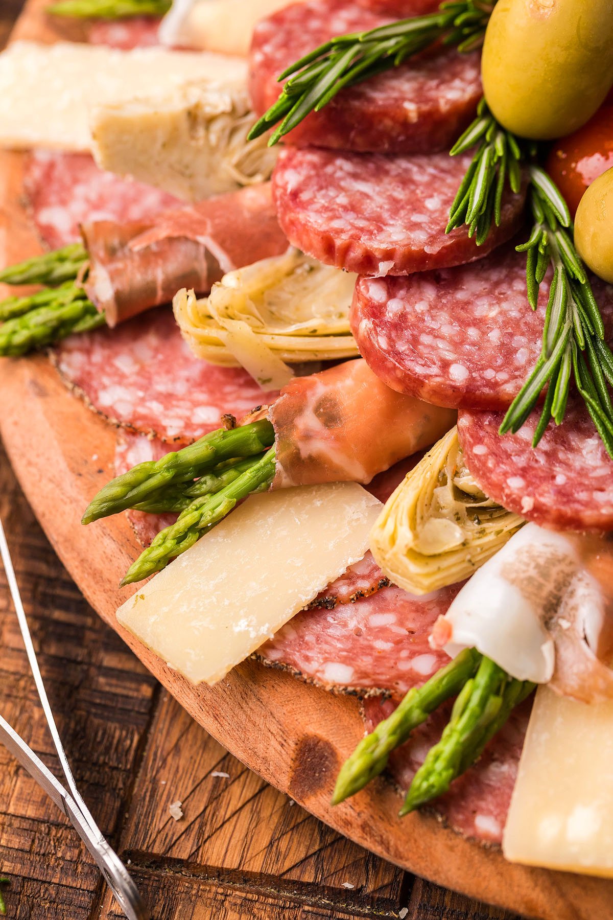 Charcuterie board with salami, cheese, asparagus, artichokes, olives, and rosemary on a wooden platter—a classic Italian starter perfect for an Italian Antipasto Board or festive Holiday Antipasto Wreath.