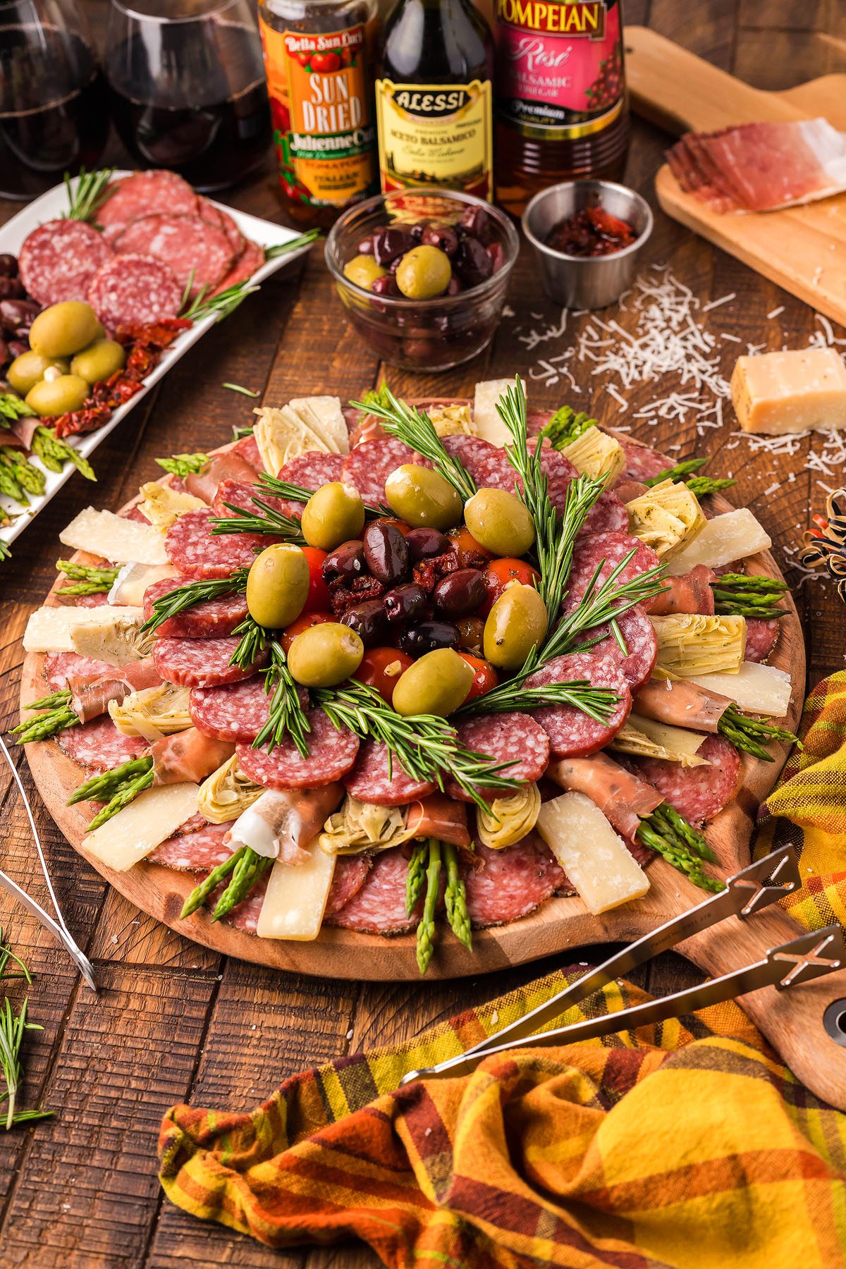A traditional Italian Antipasto Board featuring salami, olives, cheese, artichokes, asparagus, and rosemary is arranged on a wooden table—a classic Italian starter perfect for any gathering.