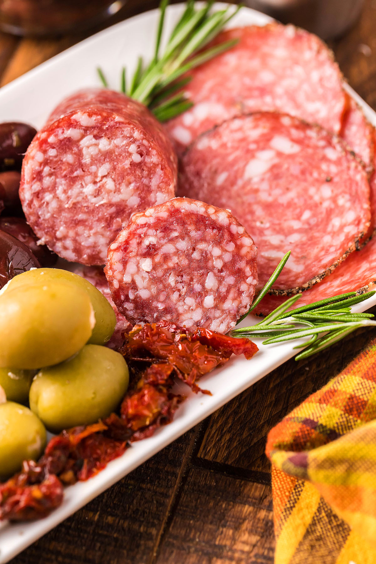 A classic Italian starter featuring sliced salami, green olives, sun-dried tomatoes, and rosemary on a white plate—perfect for any antipasto tray.