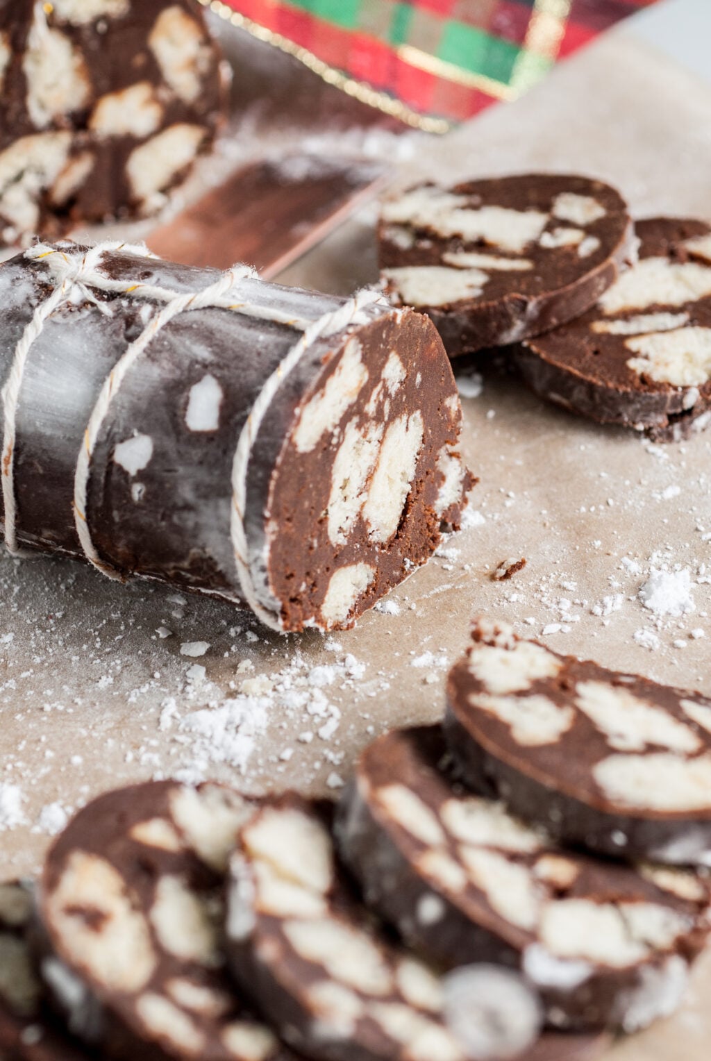 Chocolate salami slices with white biscuit pieces, dusted with powdered sugar, on parchment paper.