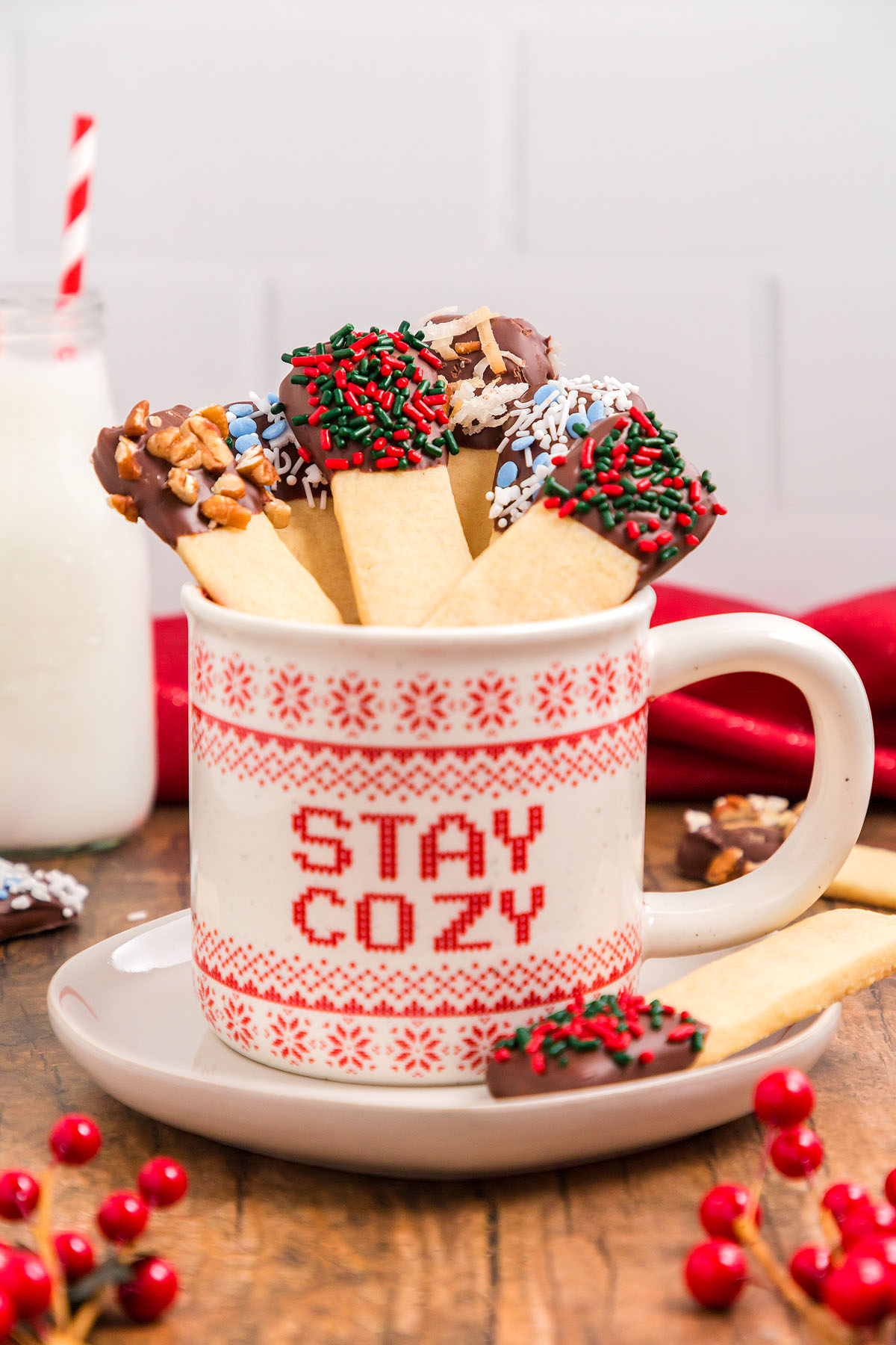A mug with "Stay Cozy" filled with chocolate-dipped shortbread cookies and Dipped Sugar Cookie Sticks, next to a glass of milk&mdash;perfect for a festive cookie exchange or a cozy treat.