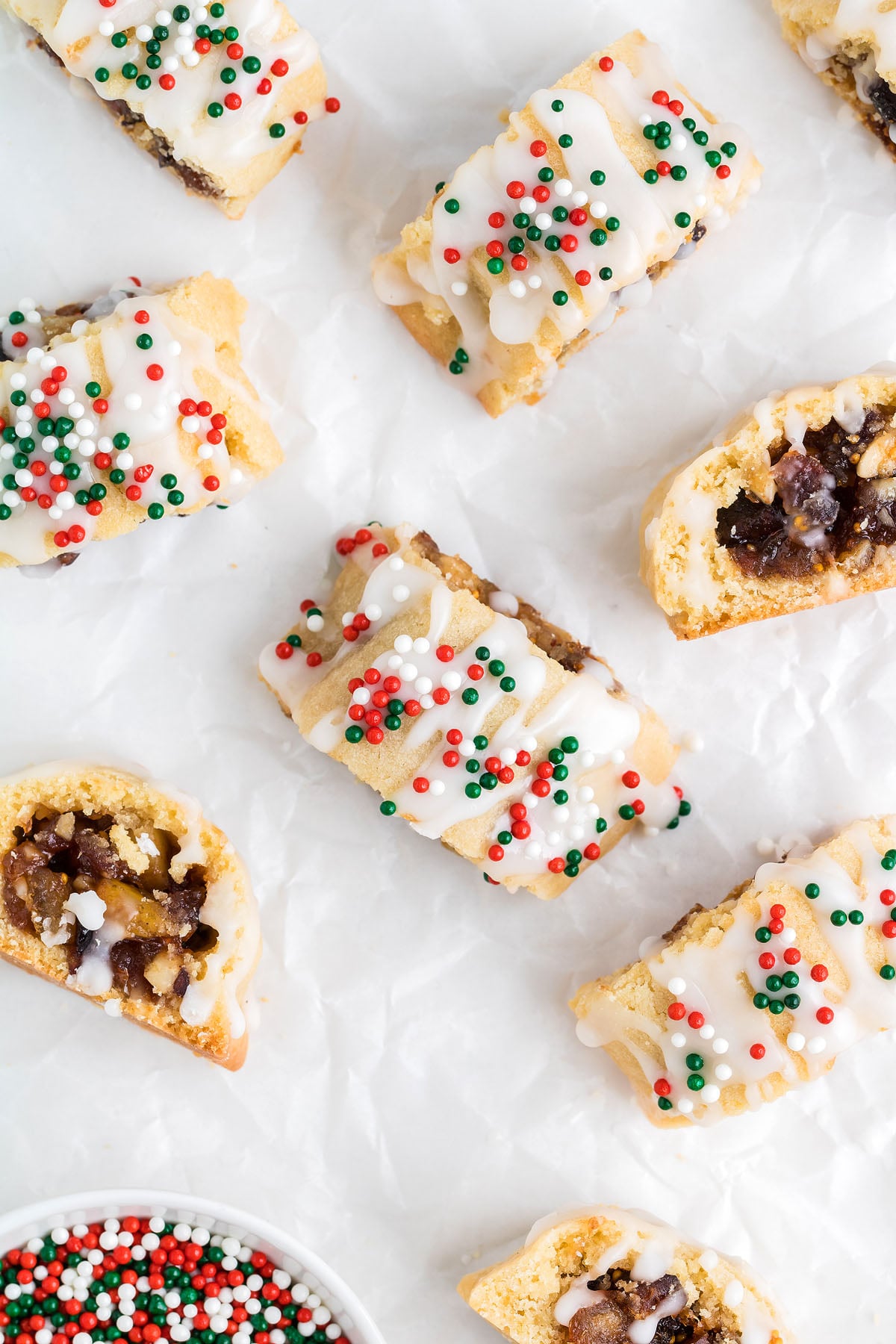 Slices of glazed biscotti topped with red, white, and green sprinkles on parchment paper, reminiscent of festive Italian Christmas cookies.