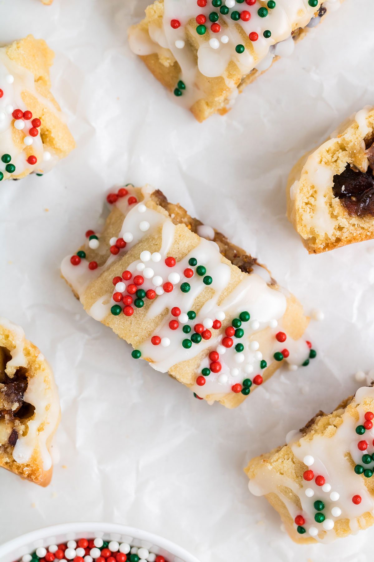 Rectangular Italian Christmas cookies with white icing and red, green, and white sprinkles rest on white parchment paper.