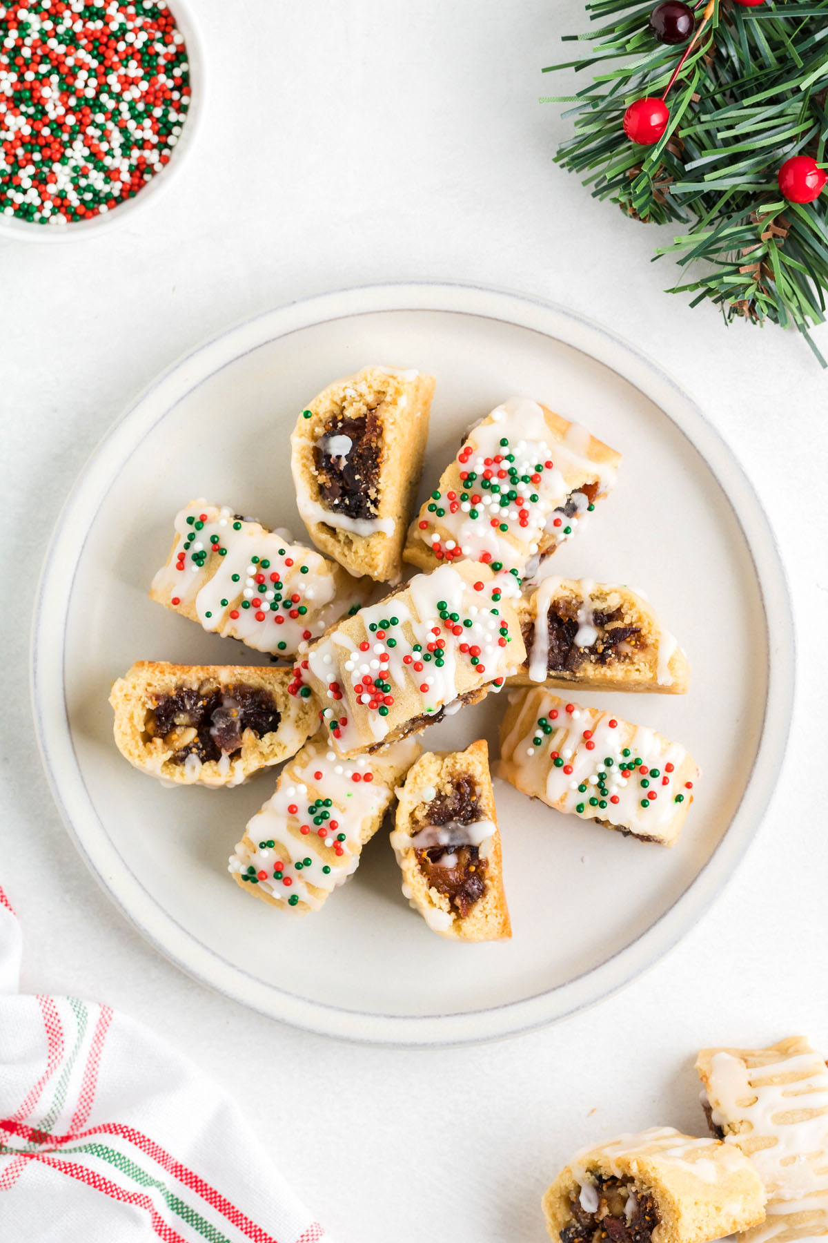 Sliced Italian Christmas cookies with icing and red, green, and white sprinkles on a plate, next to festive decor—perfect for sharing classic treats like fig cookie favorites during the holidays.
