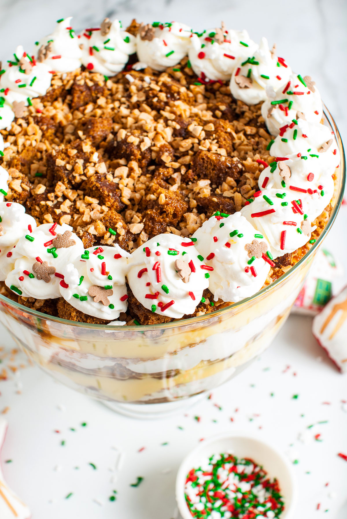 A festive Gingerbread Trifle with whipped cream, sprinkles, crumbled cake, and toffee bits makes a delightful Christmas dessert in a glass bowl.