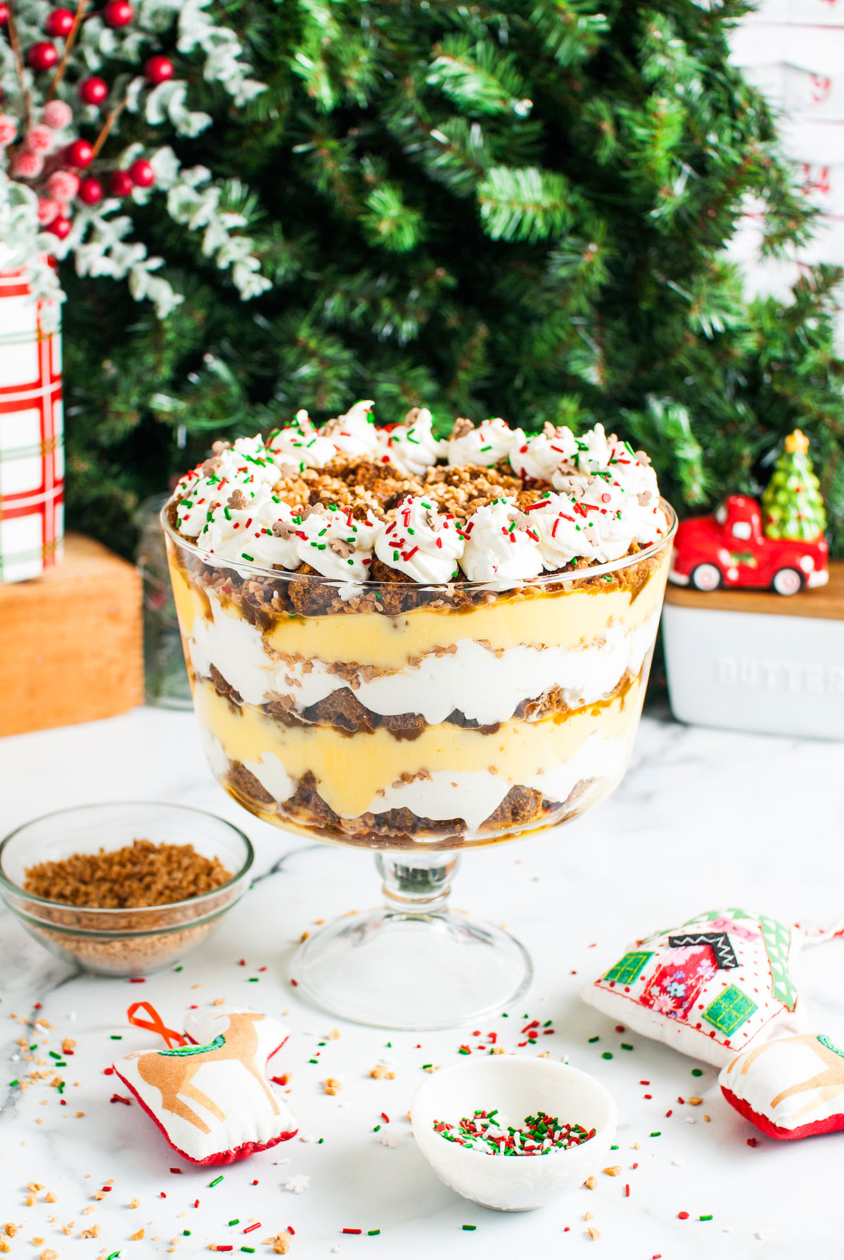 A layered Gingerbread Trifle with whipped cream, sprinkles, and cake in a glass bowl, set by festive Christmas decor—a delightful Christmas Dessert for your holiday table.