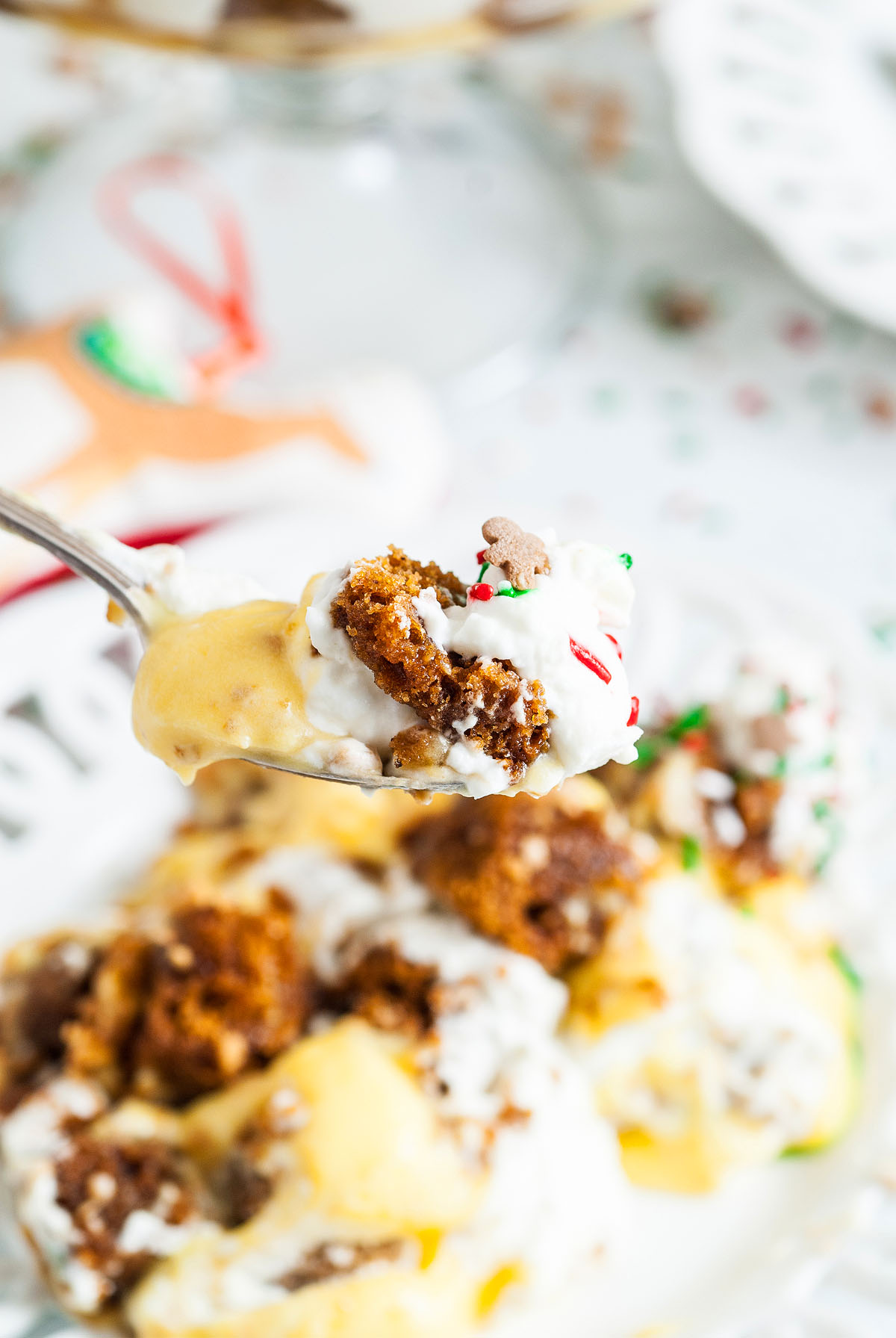 A spoonful of Gingerbread Trifle with whipped cream and sprinkles, held above a festive dessert plate—an irresistible Christmas Dessert perfect for your holiday trifle recipe collection.