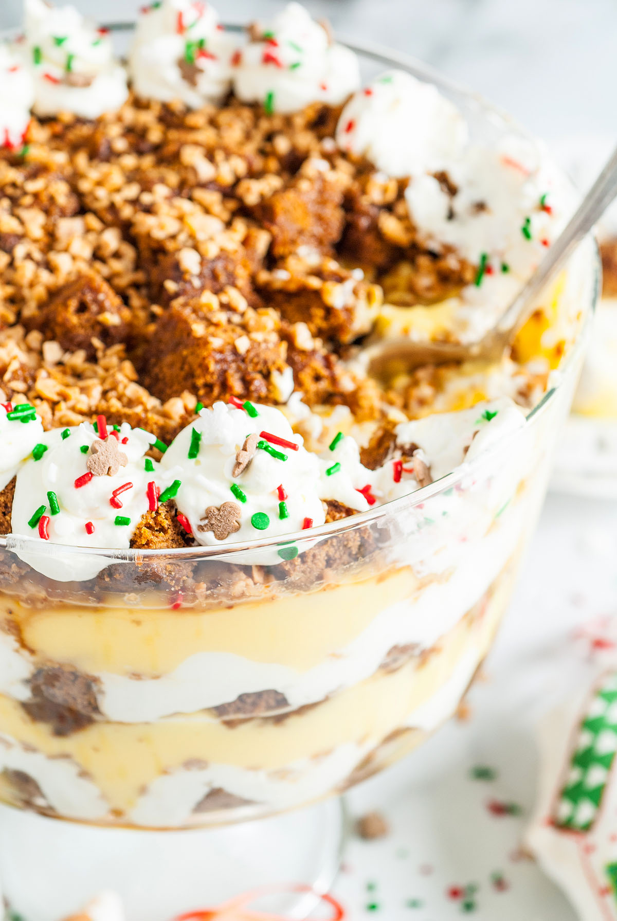 A close-up of a festive Gingerbread Trifle, a classic holiday trifle recipe with layers of whipped cream, chocolate, pudding, and colorful holiday sprinkles on top.