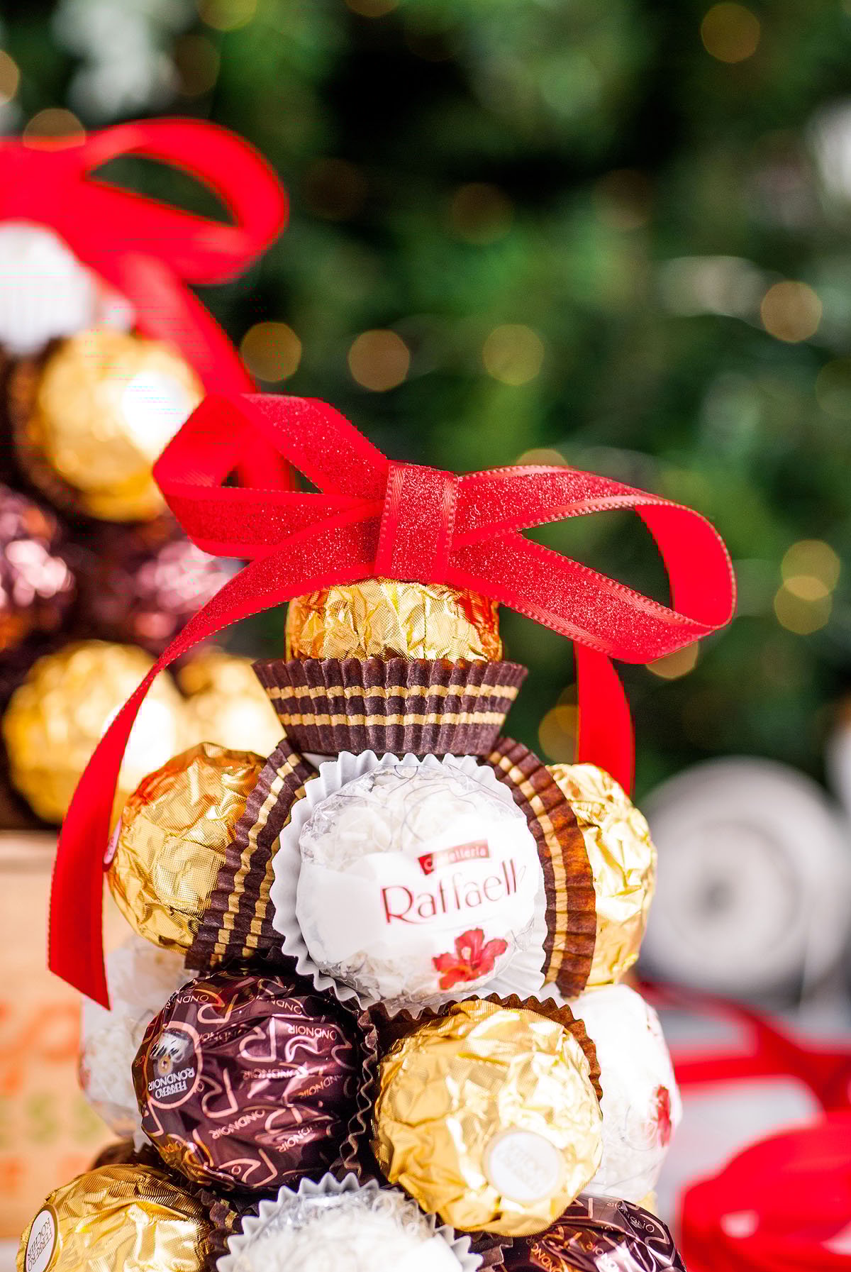 A festive candy arrangement with chocolates and a red ribbon, set against a blurred Christmas tree background—the perfect DIY Christmas decoration or thoughtful Christmas hostess gift.