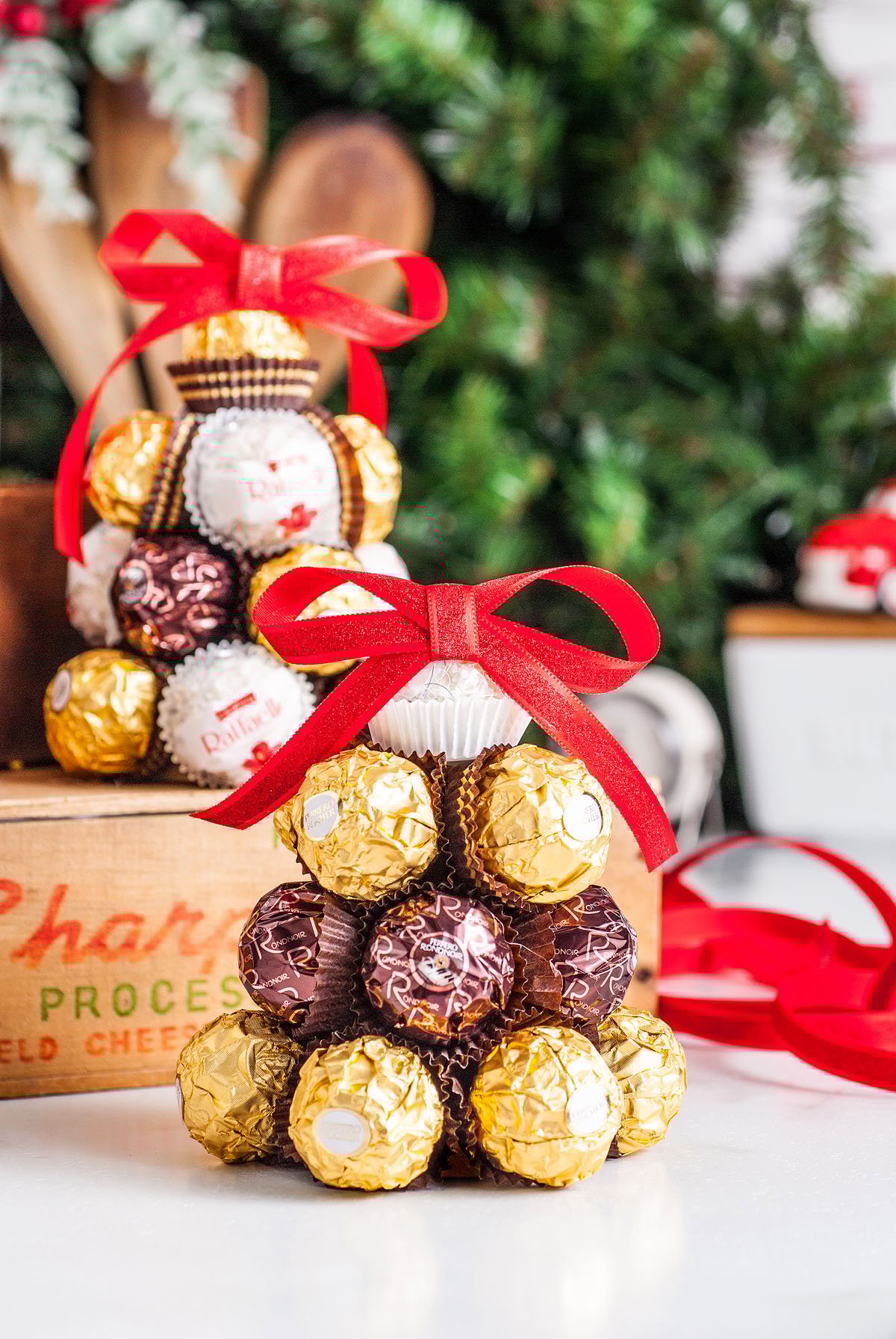 Homemade Ferrero Rocher Christmas Tree candies are stacked in a pyramid, topped with a red bow, making the perfect DIY Christmas decoration against a festive holiday background.