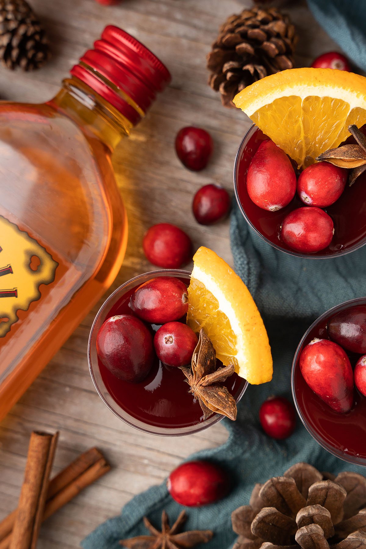 Festive drinks with cranberries, orange slices, and star anise beside a bottle on a wooden table—perfect inspiration for Mulled Wine Fireball Jello Shots or other creative Christmas shot recipes.
