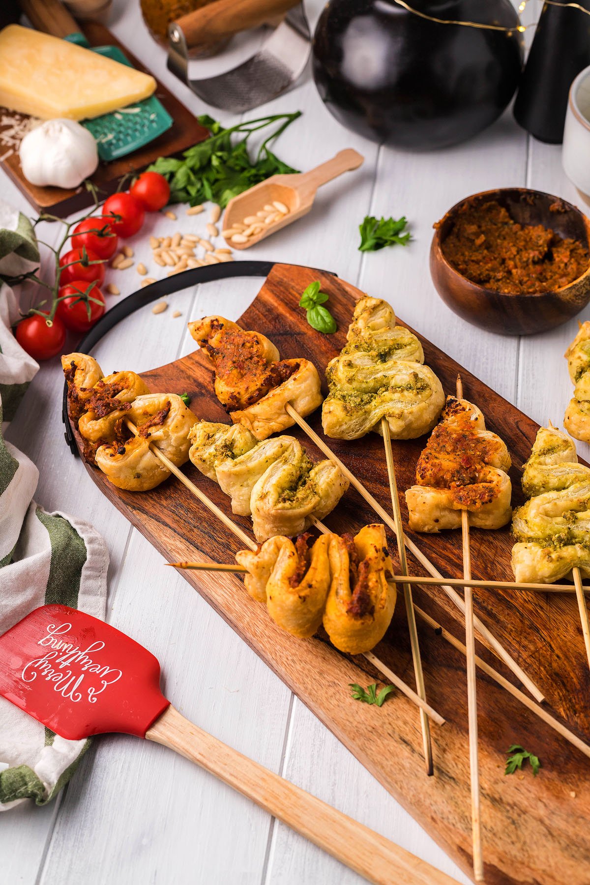 Pastry twists on wooden skewers with green and red fillings, displayed on a wooden board with fresh ingredients nearby—perfect as festive Christmas appetizers or as part of your favorite puff pastry recipe.