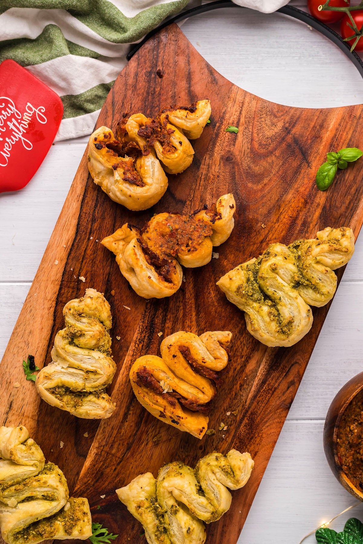 Assorted puff pastry twists with pesto and tomato toppings on a wooden serving board—perfect as festive Christmas appetizers or for trying a new puff pastry recipe.