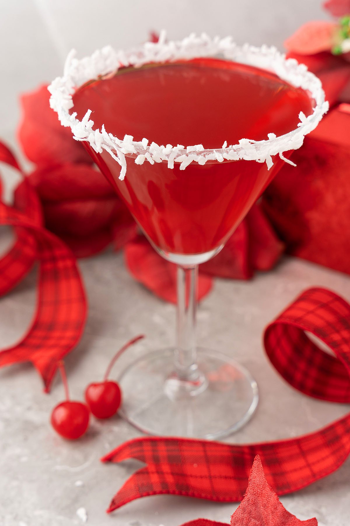 A festive Red Christmas Cocktail, this Santa’s Hat Coconut Rum Cocktail features a vibrant red drink in a martini glass rimmed with coconut, garnished with cherries and wrapped in holiday ribbons for the perfect holiday drink.