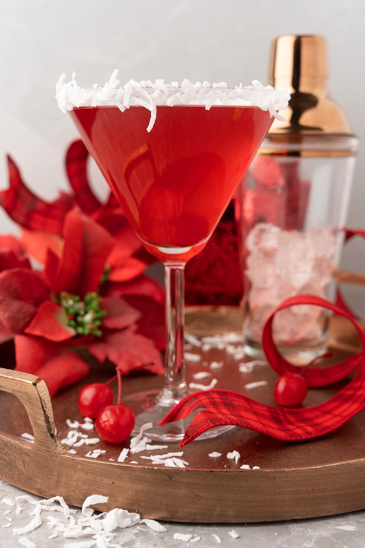 A festive Red Christmas Cocktail, the Santa’s Hat Coconut Rum Cocktail is served in a martini glass rimmed with coconut and garnished with cherries and holiday decorations.