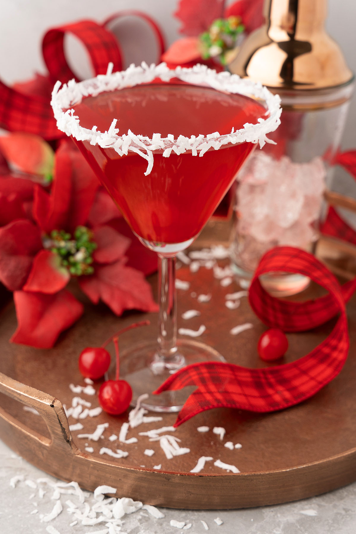 A festive red christmas cocktail in a martini glass with a shredded coconut rim, garnished with cherries and red ribbon. This Santa’s Hat Coconut Rum Cocktail is the perfect holiday drink for your seasonal celebrations.