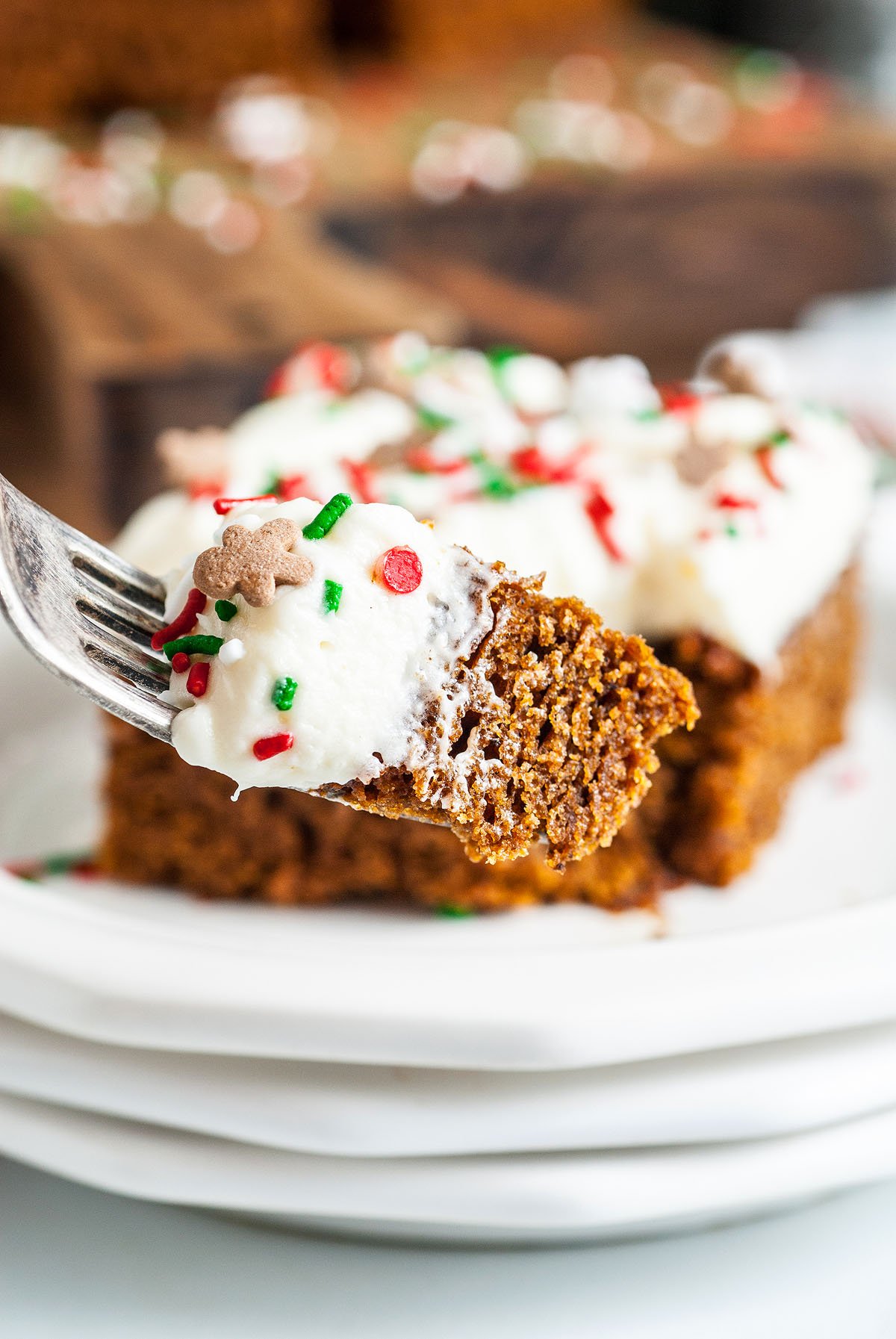 A fork holds a bite of old fashioned gingerbread cake with white frosting and colorful holiday sprinkles—perfect as a festive fall or holiday dessert.