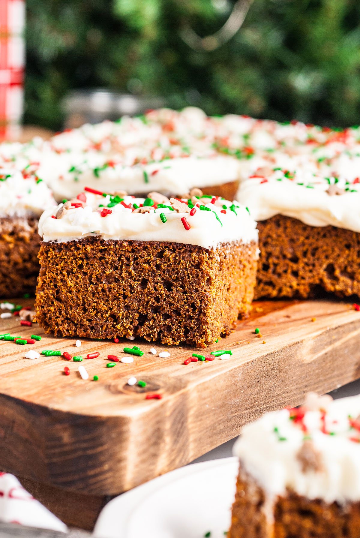 Square slices of old fashioned gingerbread cake with white frosting and colorful sprinkles sit on a wooden board, perfect as a festive fall or holiday dessert.