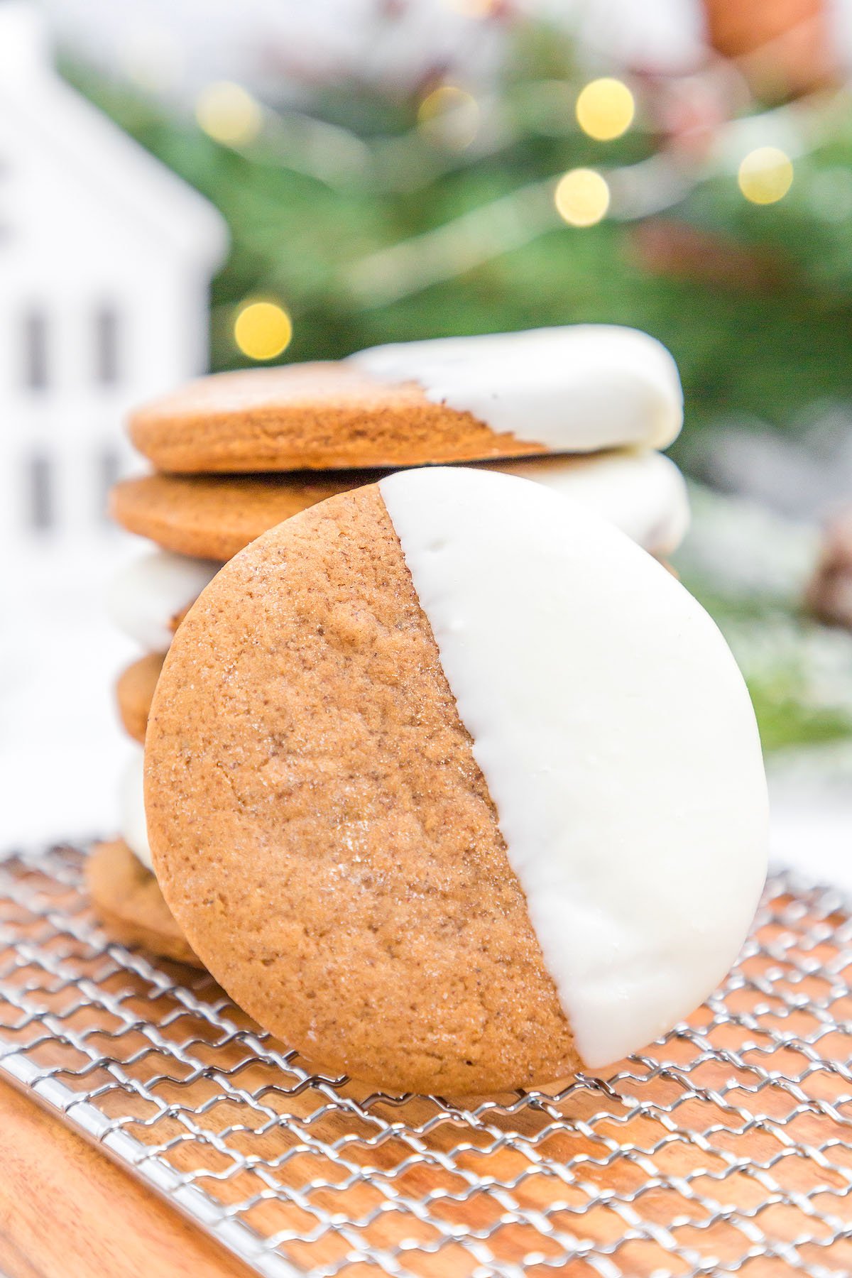 A round white chocolate dipped ginger cookie stands in front of a stack of similar cookies, its half-dipped icing glistening.
